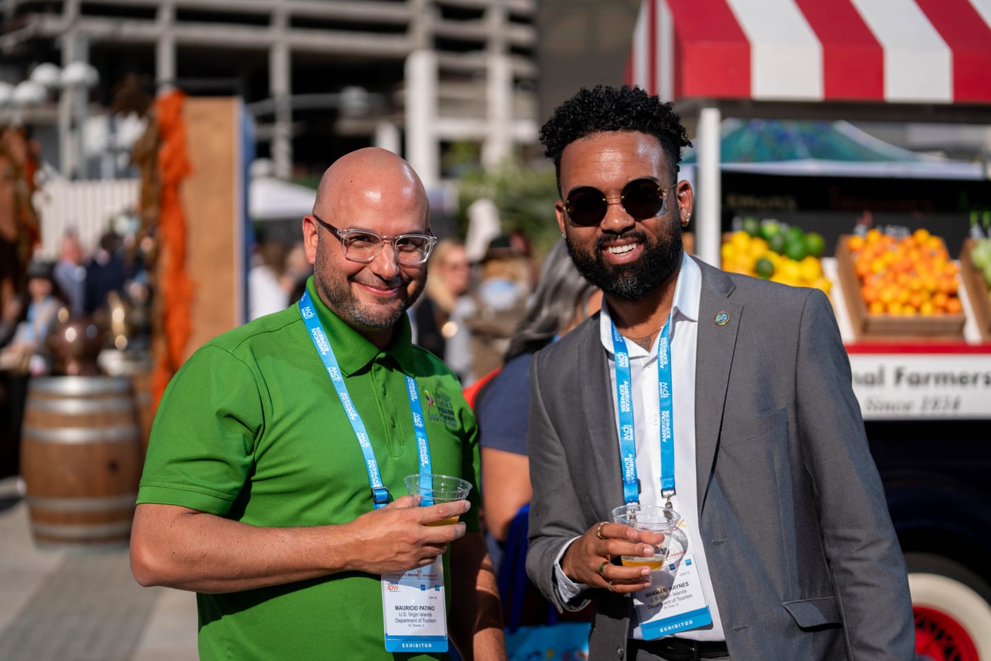 Two IPW delegates with drinks in hand at an outdoor reception beside a farmers-market style stall