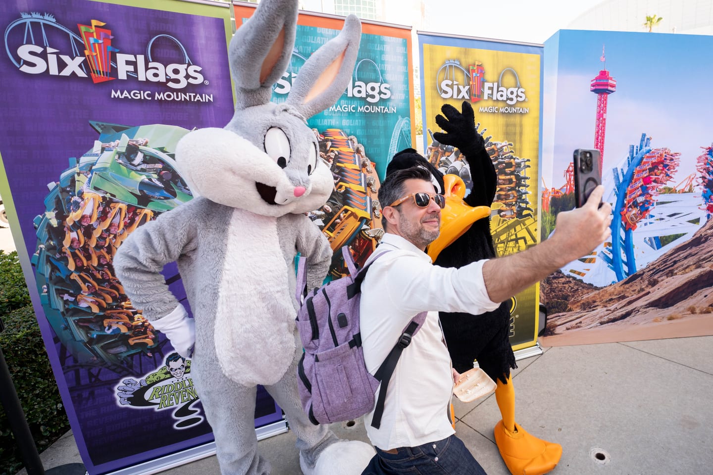 A delegate taking a selfie with Bugs Bunny and Daffy Duck in front of Six Flags Magic Mountain banners at IPW