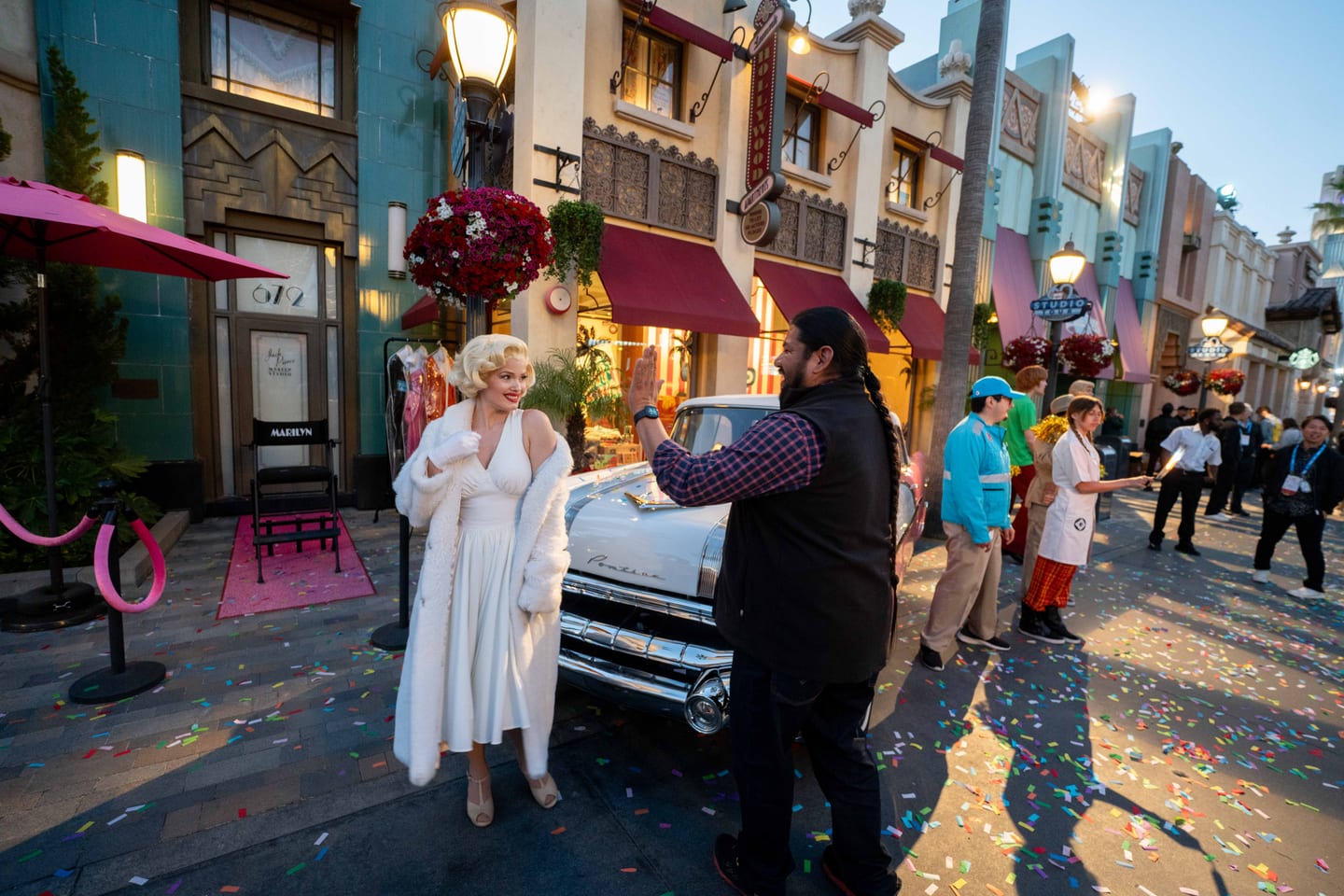 A Marilyn Monroe lookalike posing beside a vintage convertible on a Universal Studios backlot street strewn with confetti