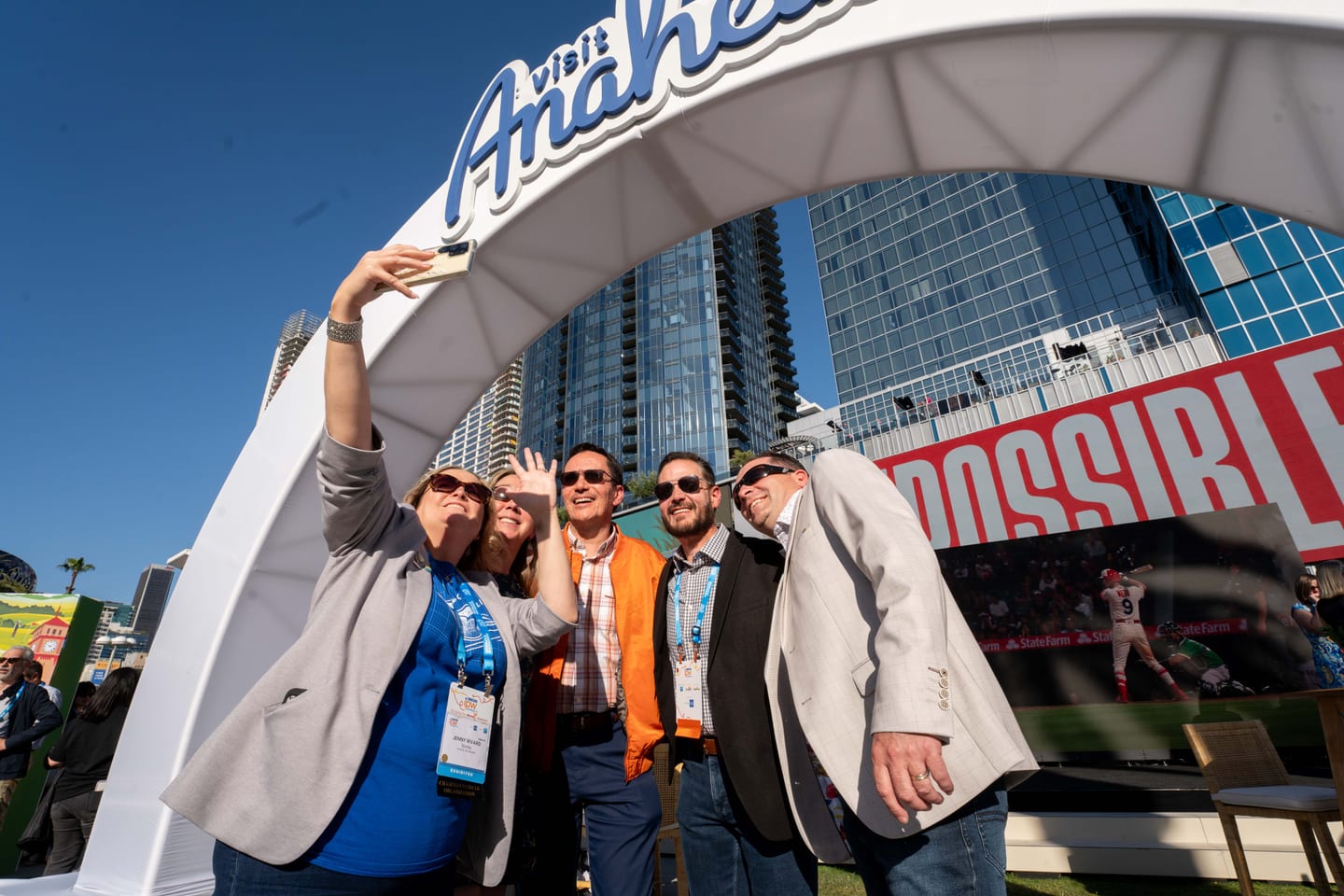 Four delegates taking a selfie under a white Visit Anaheim arch with downtown Los Angeles behind them at IPW