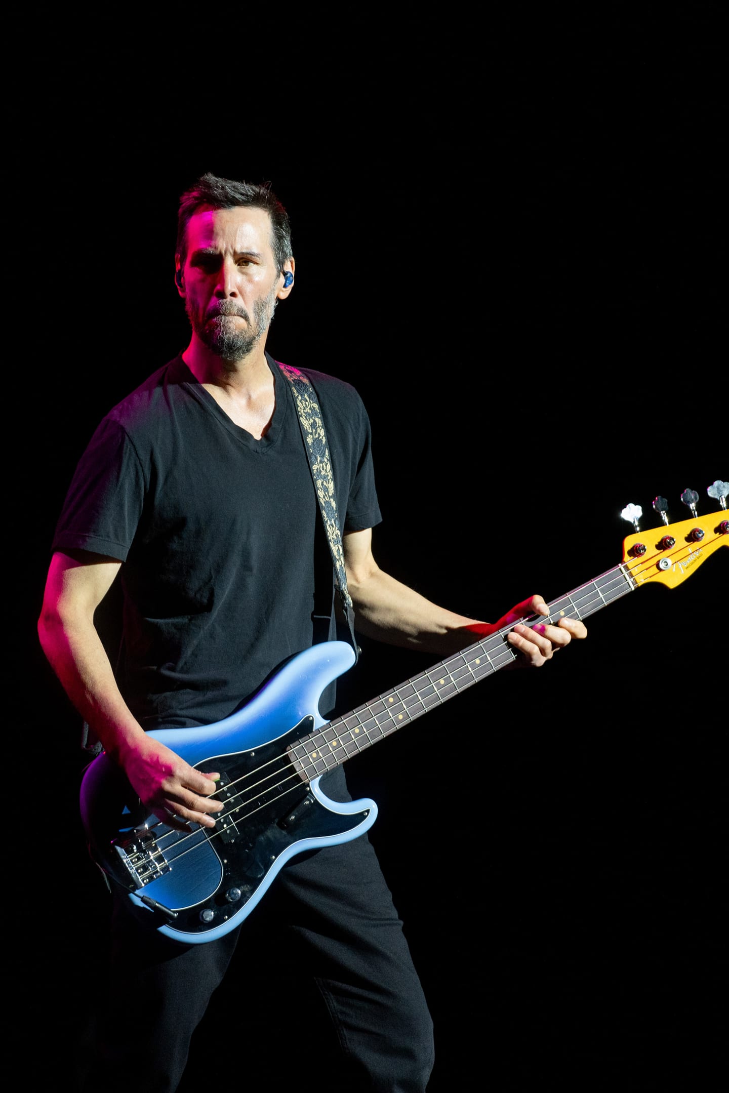 Keanu Reeves playing a blue bass guitar with his band Dogstar under stage lights on IPW opening night