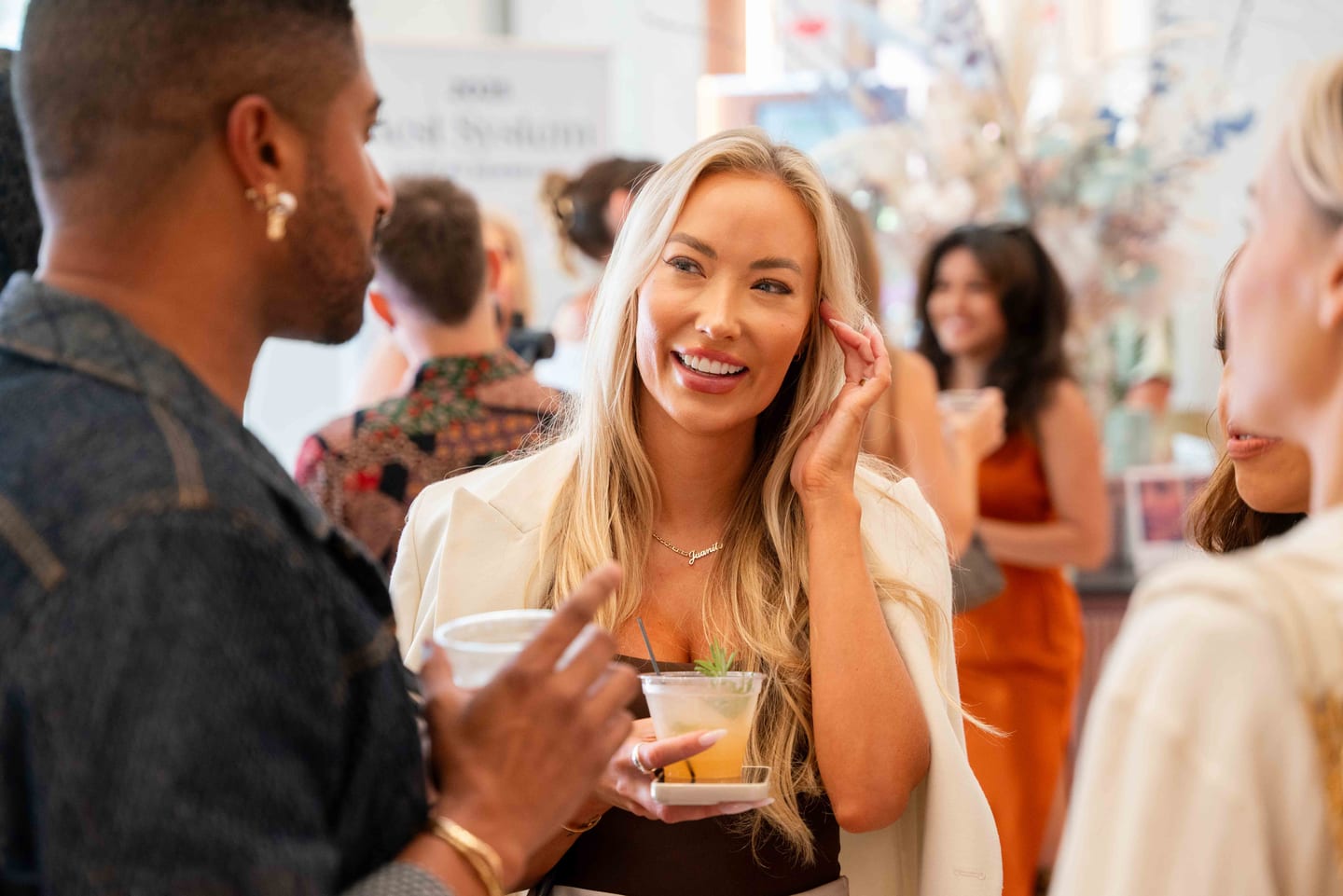 A guest smiling in conversation with a drink at the Marini skincare pop-up