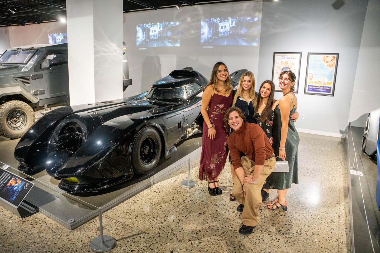 Five guests in cocktail attire posing beside the 1989 Batmobile in the Hollywood Dream Machines gallery at the Petersen Automotive Museum