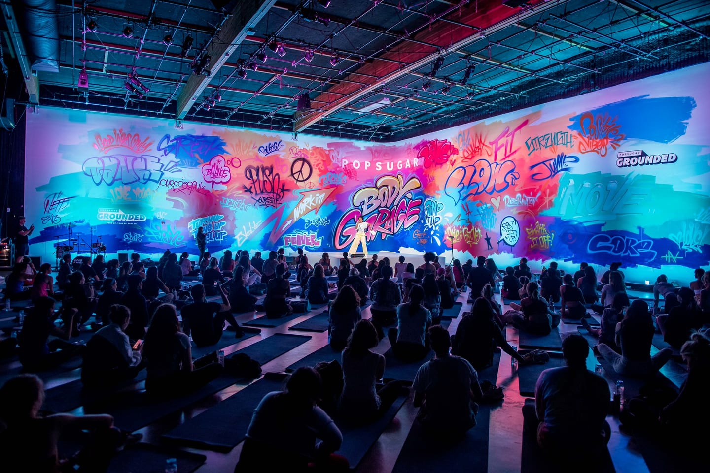 Crowd on yoga mats before a giant graffiti-mural projection at a POPSUGAR wellness activation