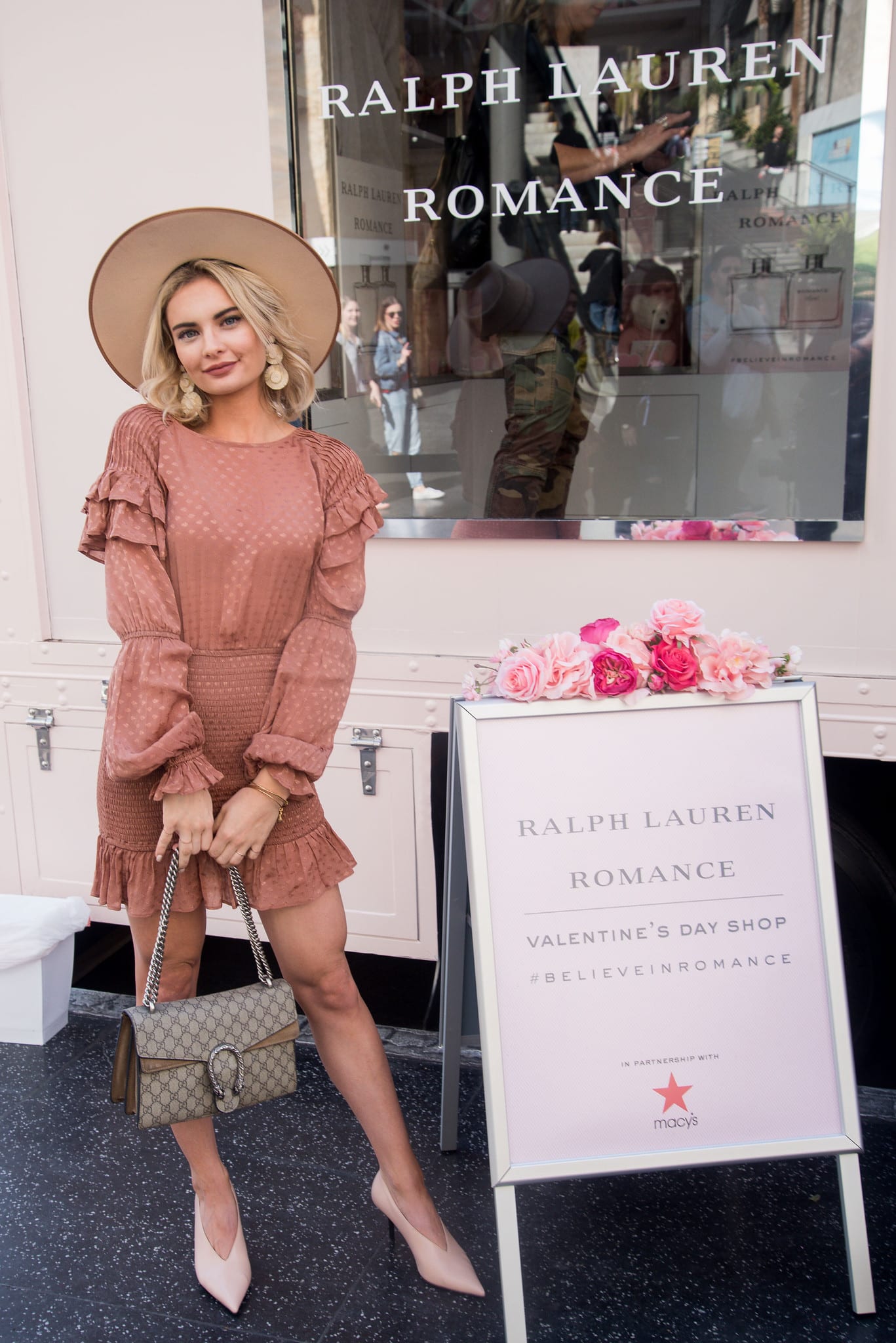 A guest in a hat posing beside the Ralph Lauren Romance Valentine’s shop signage and fragrance window