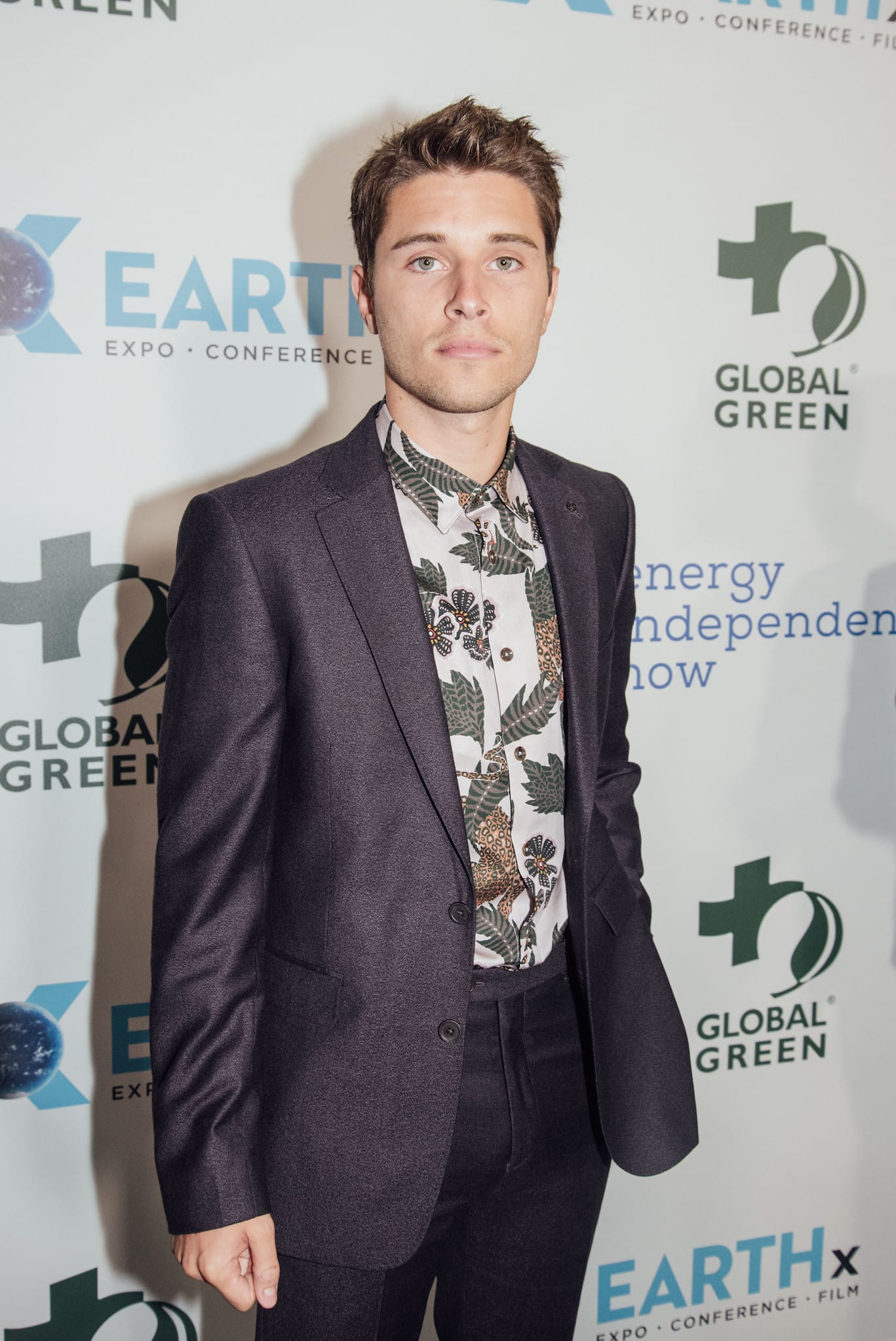 Actor Ronen Rubinstein in a plum suit and floral shirt on the green carpet at the Global Green pre-Oscar gala