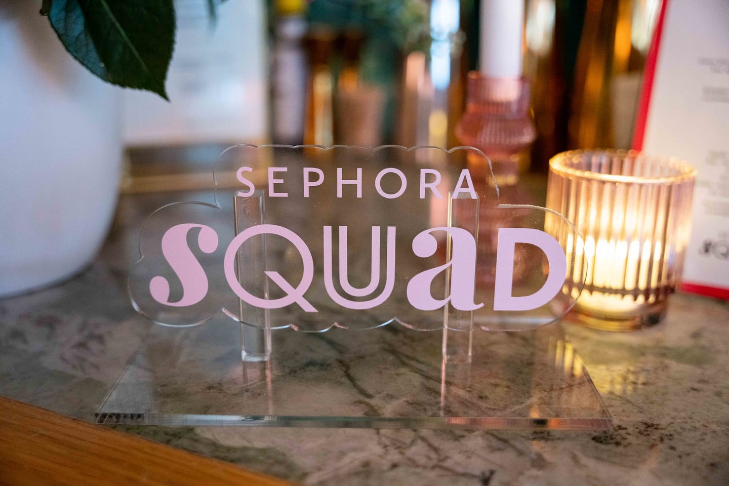 A Sephora Squad acrylic sign on a marble table beside a candle at a beauty brand event