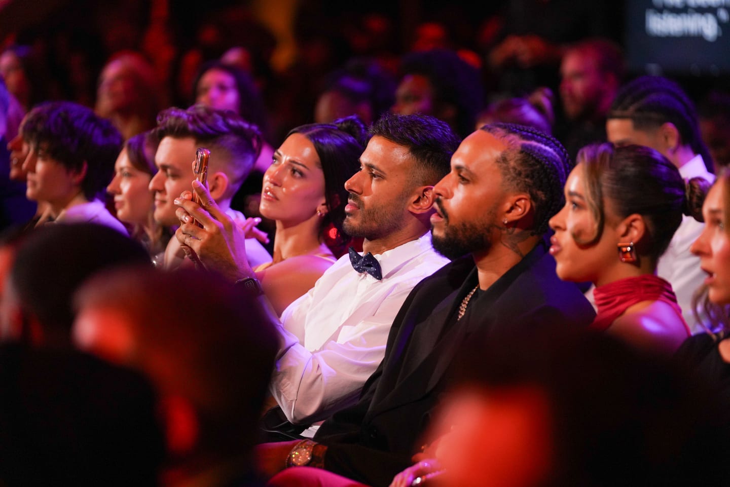 The seated audience applauding in pink and purple light