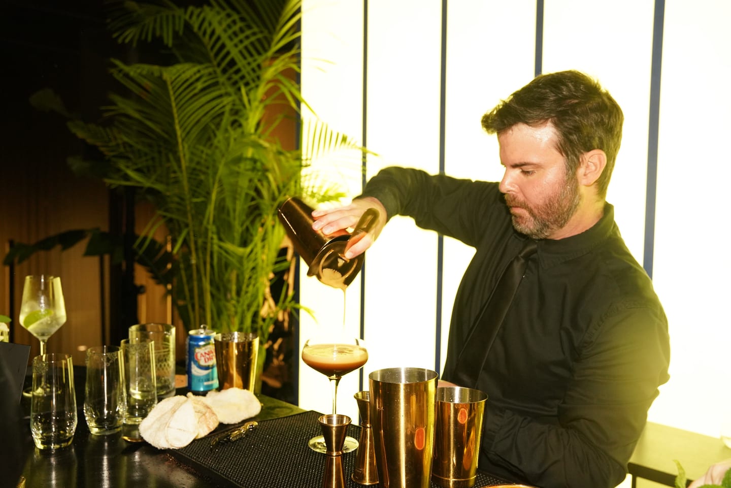 A bartender pouring a cocktail into gold glassware