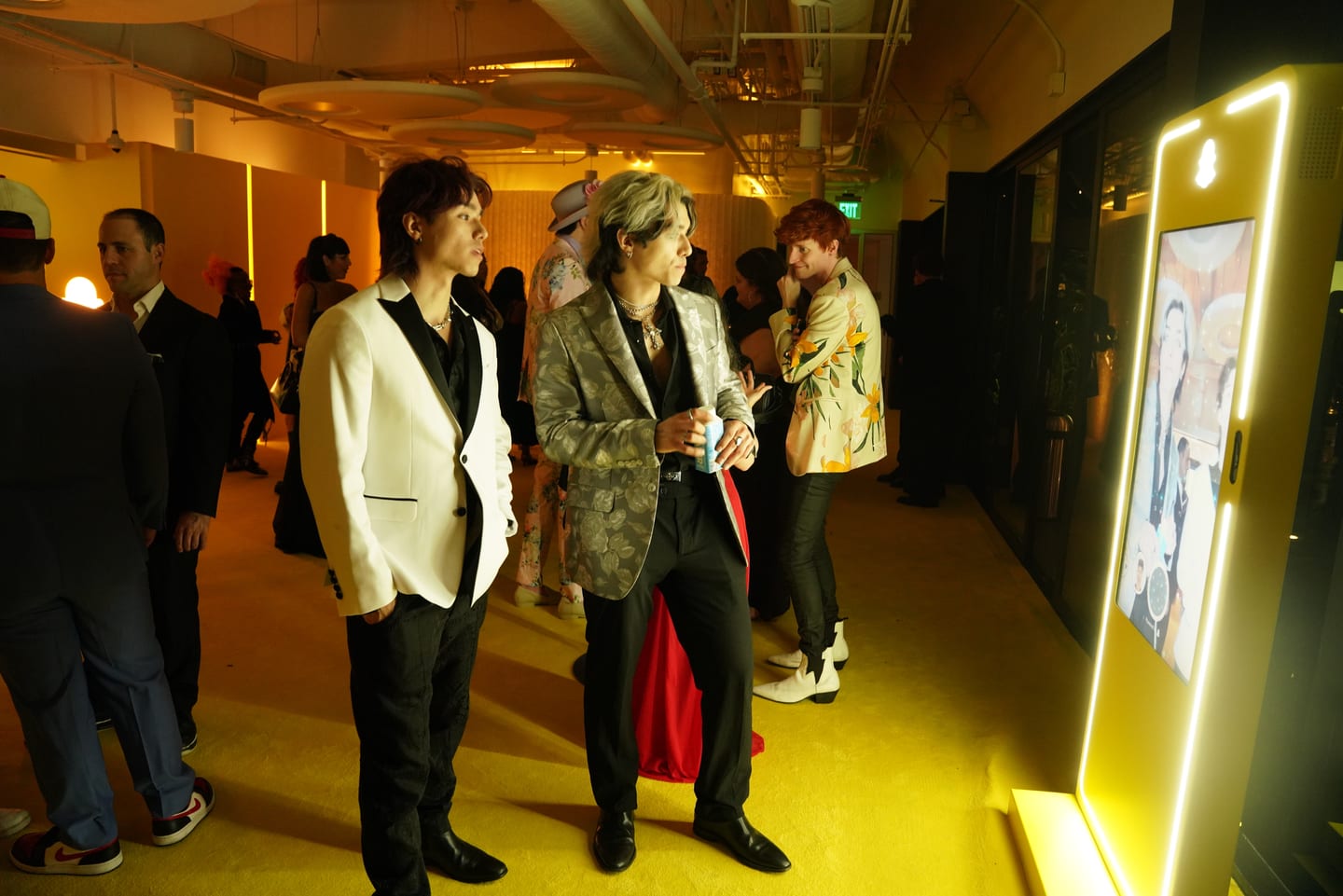 Guests in a yellow-lit corridor beside an illuminated screen