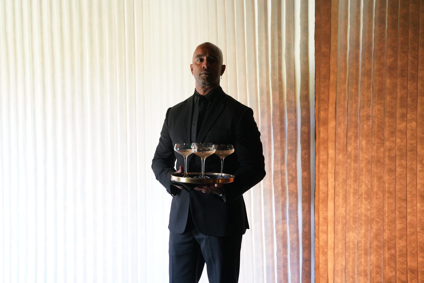 A server carrying a tray of cocktails past a curtained wall