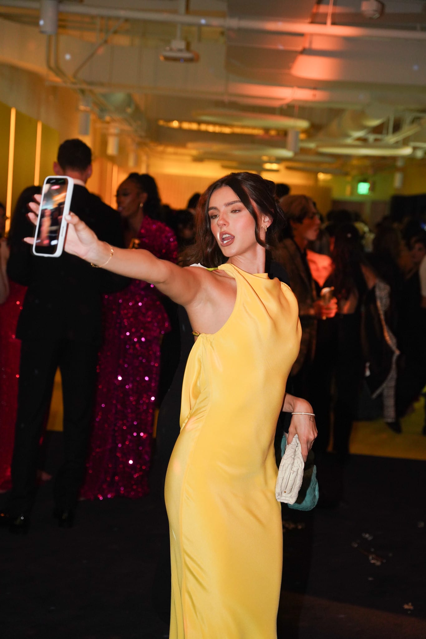 A guest in a yellow gown photographing another guest on her phone
