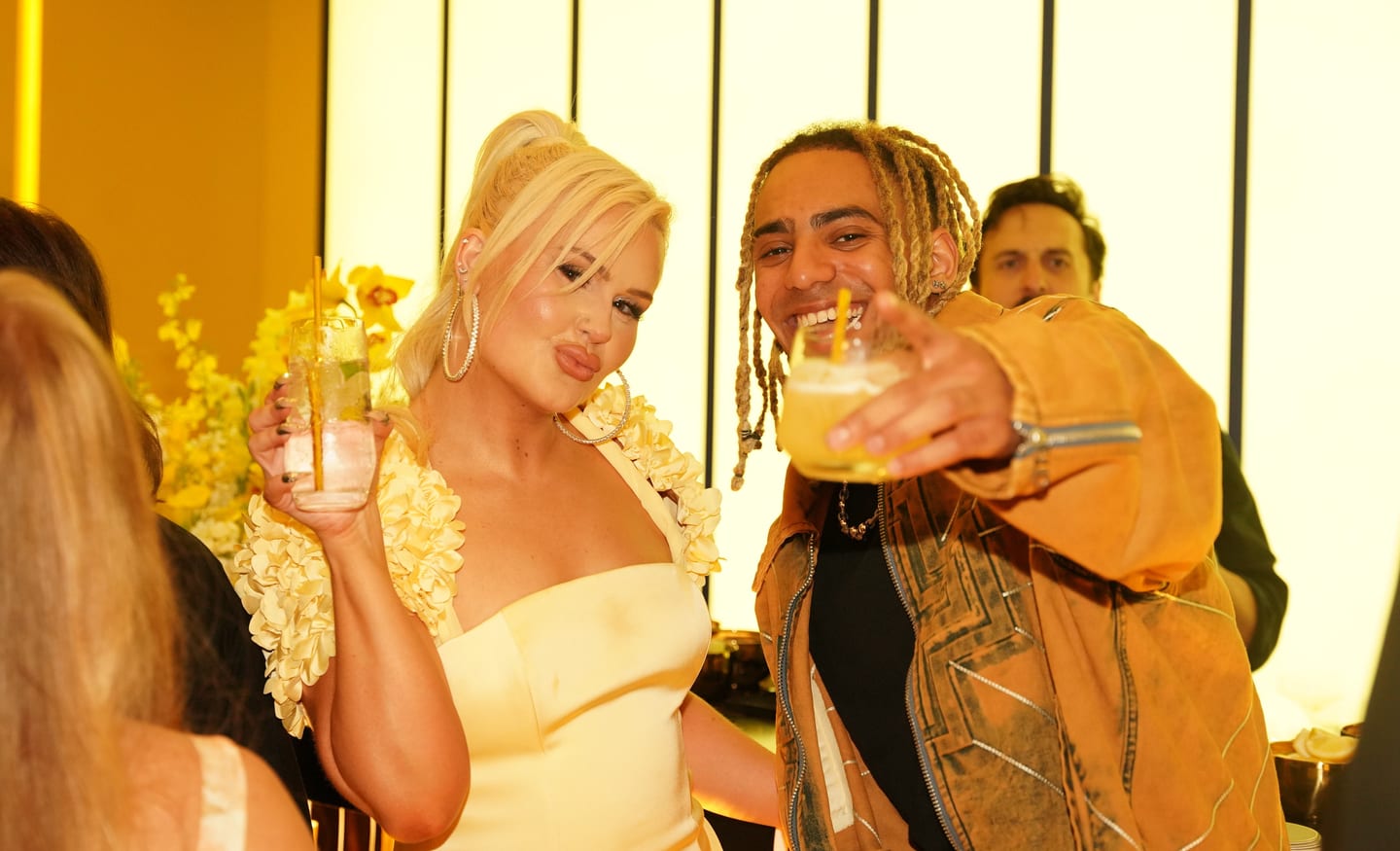 Two guests raising cocktails together beside yellow florals