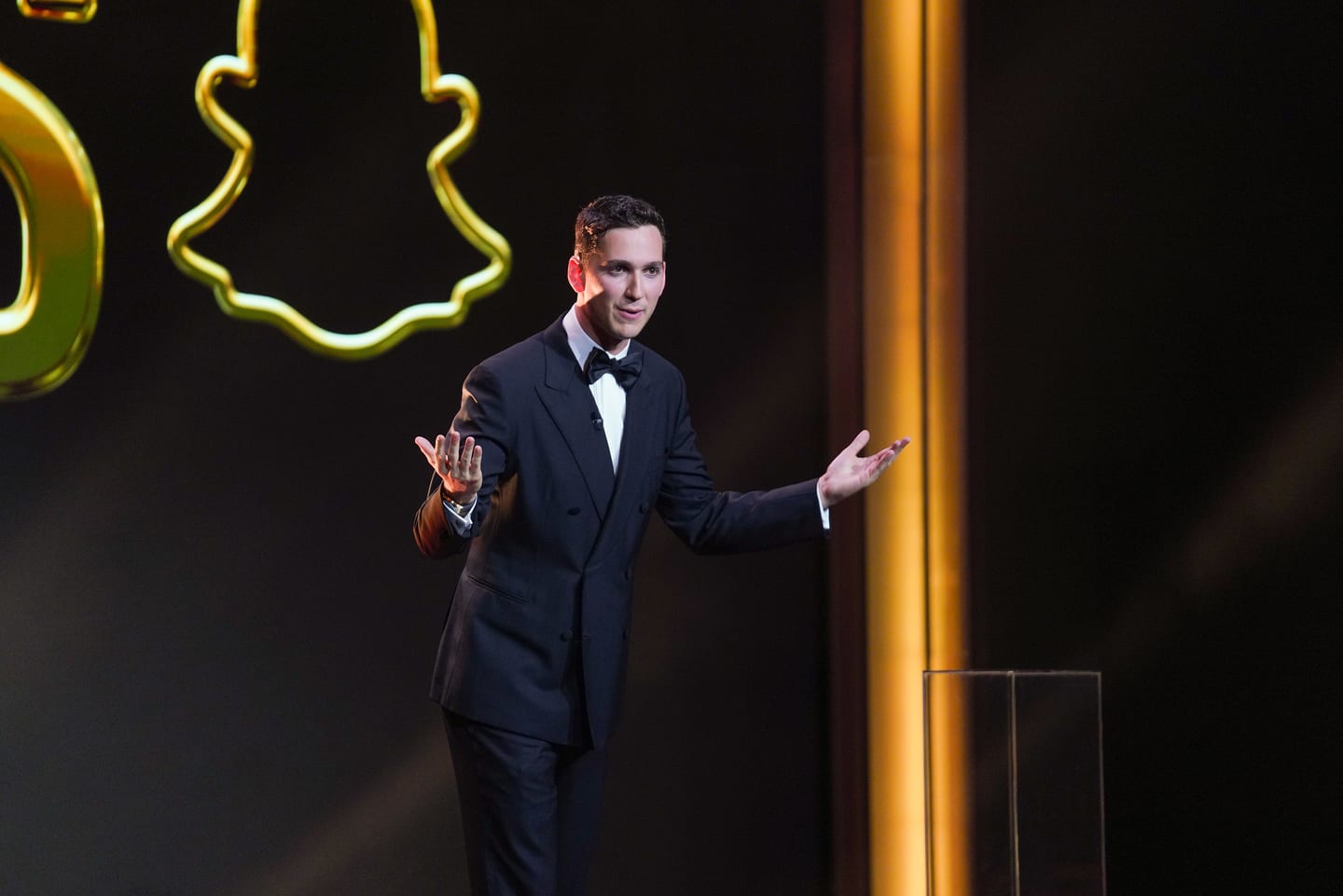 A host in a navy tuxedo on stage in front of a neon Snapchat ghost outline
