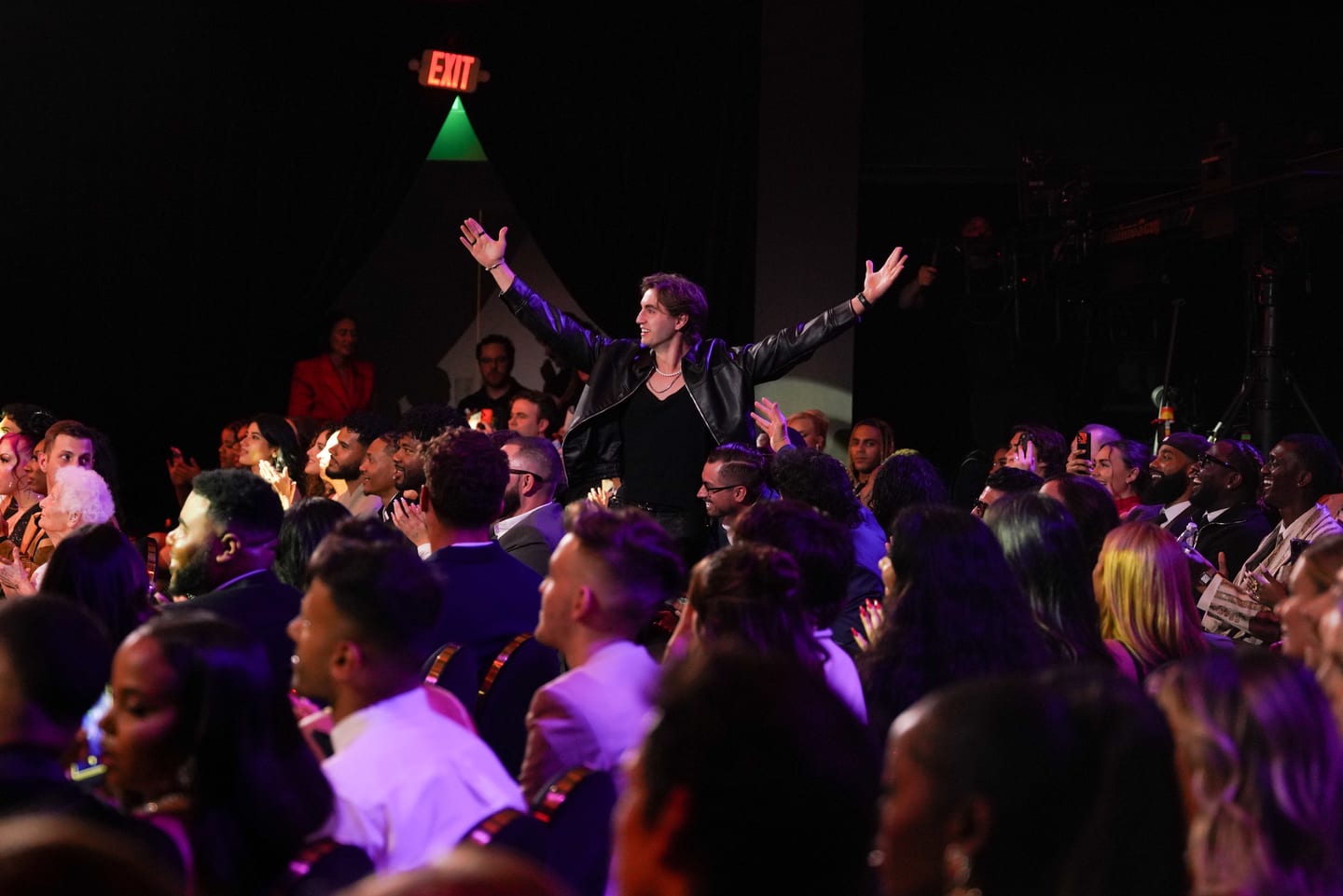 A performer with arms raised above the crowd in purple light