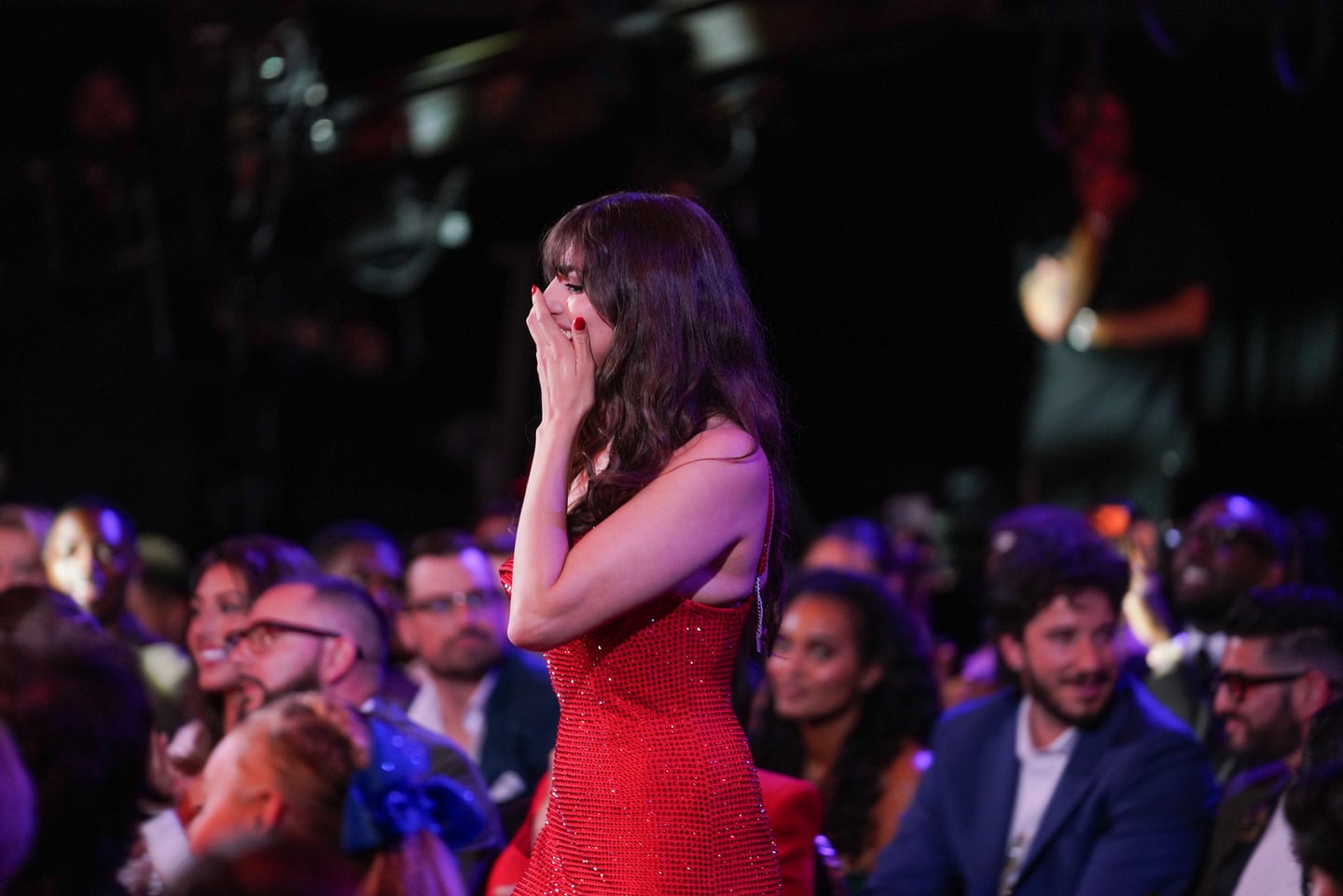 A guest in a red dress walking through the seated audience