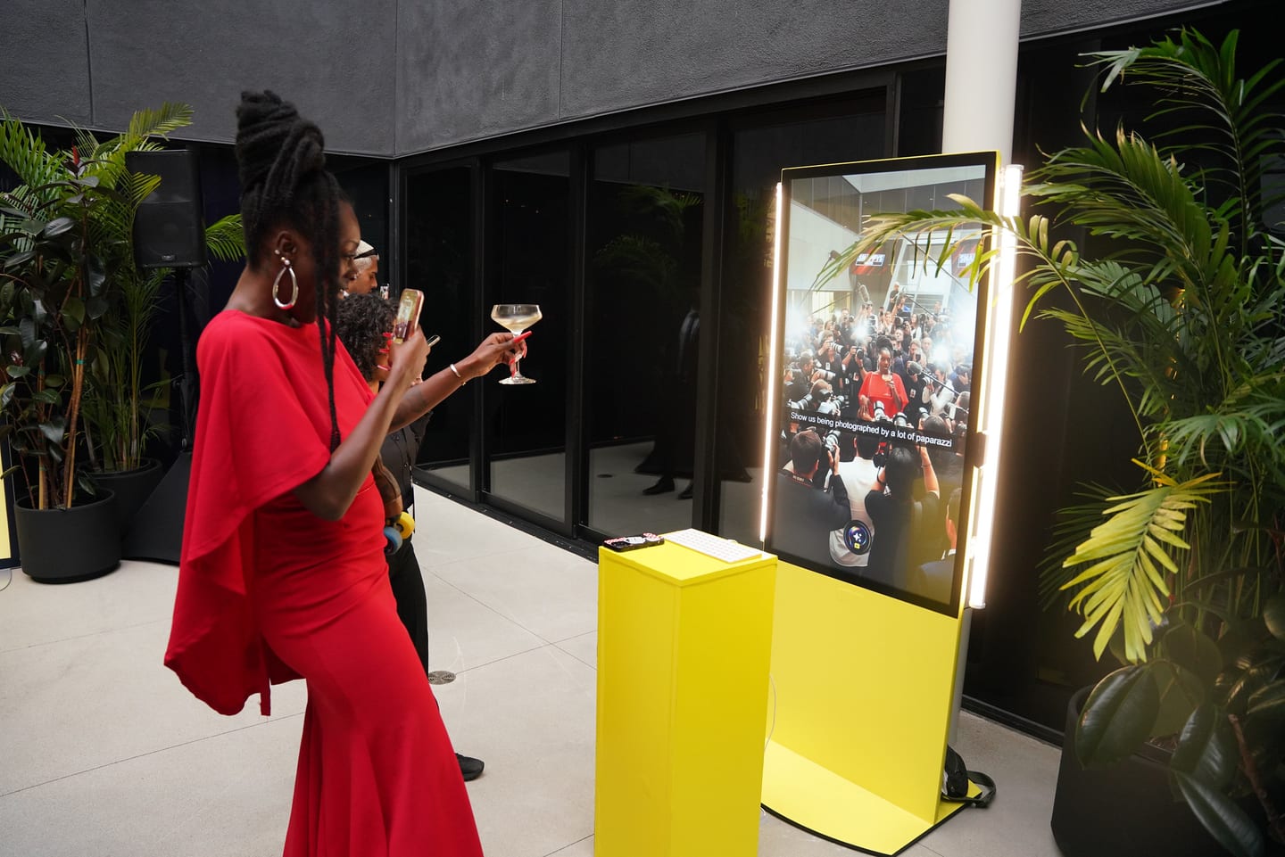 A guest in a red gown with a drink beside a lit vertical screen