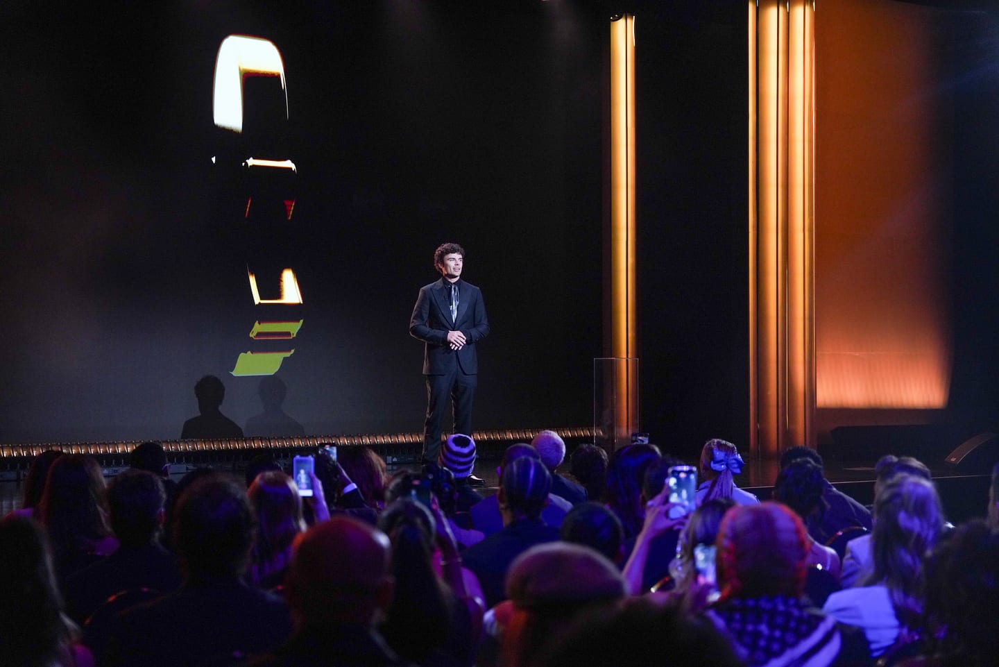 A speaker alone in a spotlight on the darkened stage above the audience