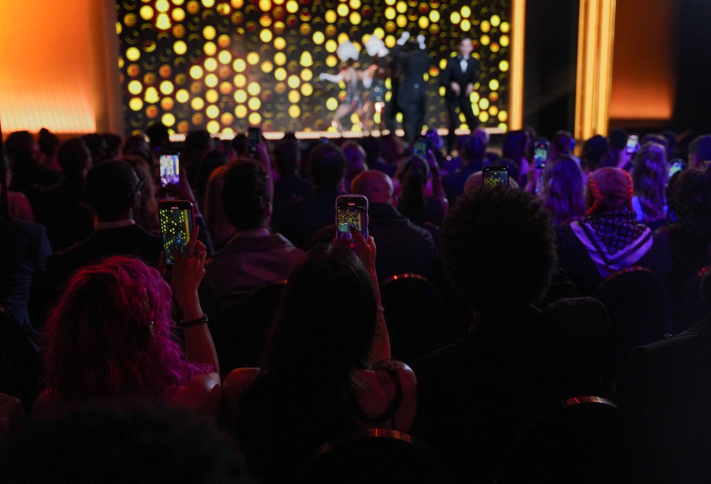 The audience filming a performance on their phones, lit by a wall of glowing gold discs behind the performers on stage at the SNAPPYS, Snapchat’s creator awards