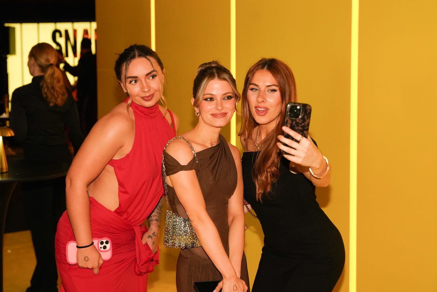 Three guests posing for a phone selfie against gold slats