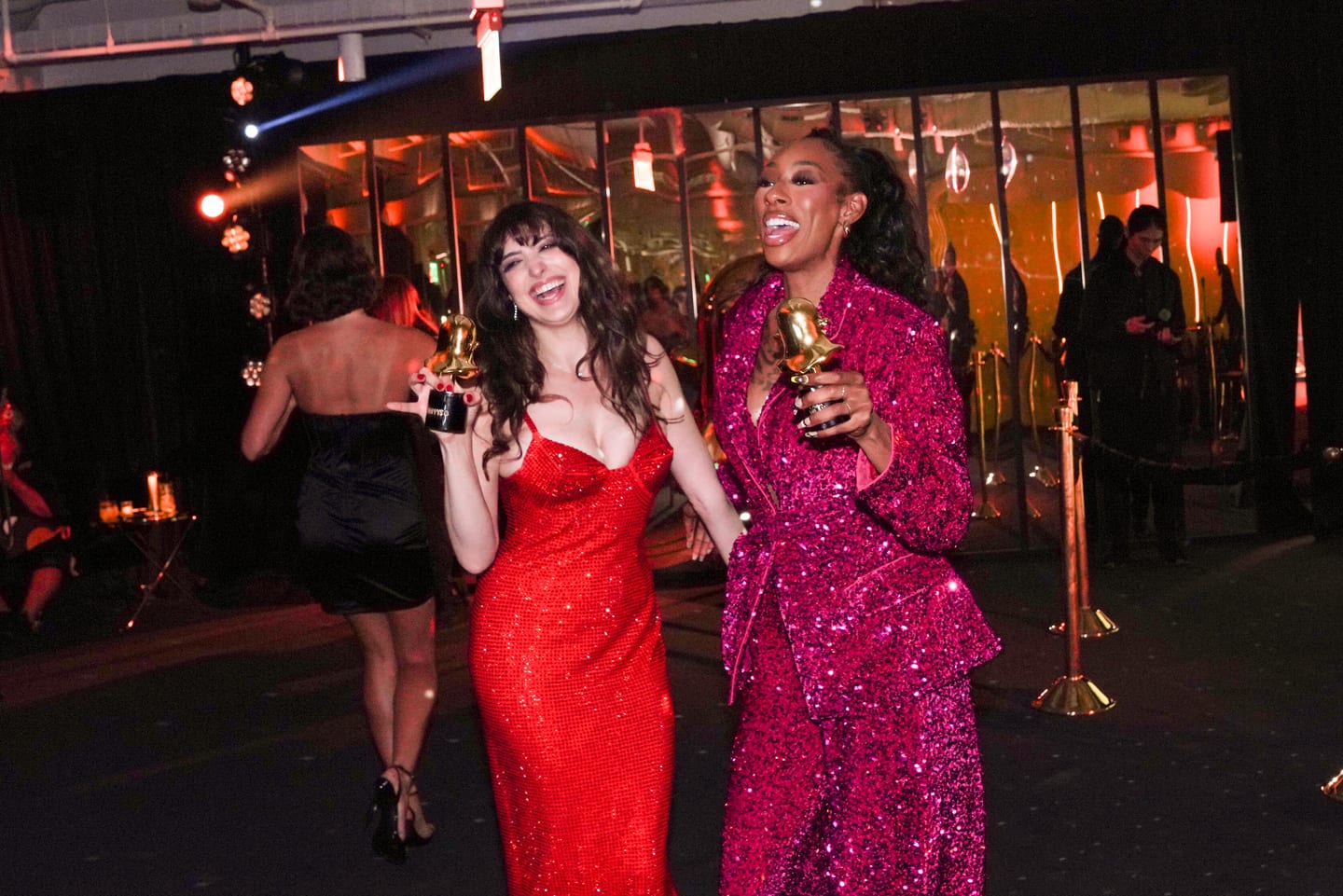 Two guests in gowns carrying gold trophies outside after the show