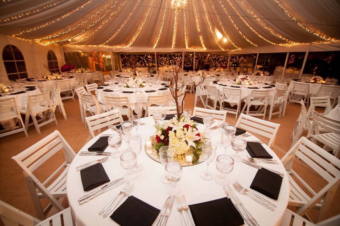 Elegant tented gala dinner with round tables and string lights at an event