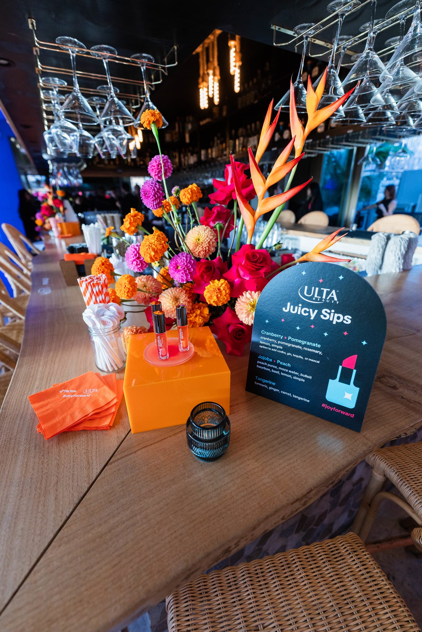 A rooftop bar dressed with a tall tropical floral arrangement and an Ulta Beauty Juicy Sips drinks menu card at the TikTok and Ulta Beauty #TikTokBeauty dinner on the LouLou rooftop in Santa Monica