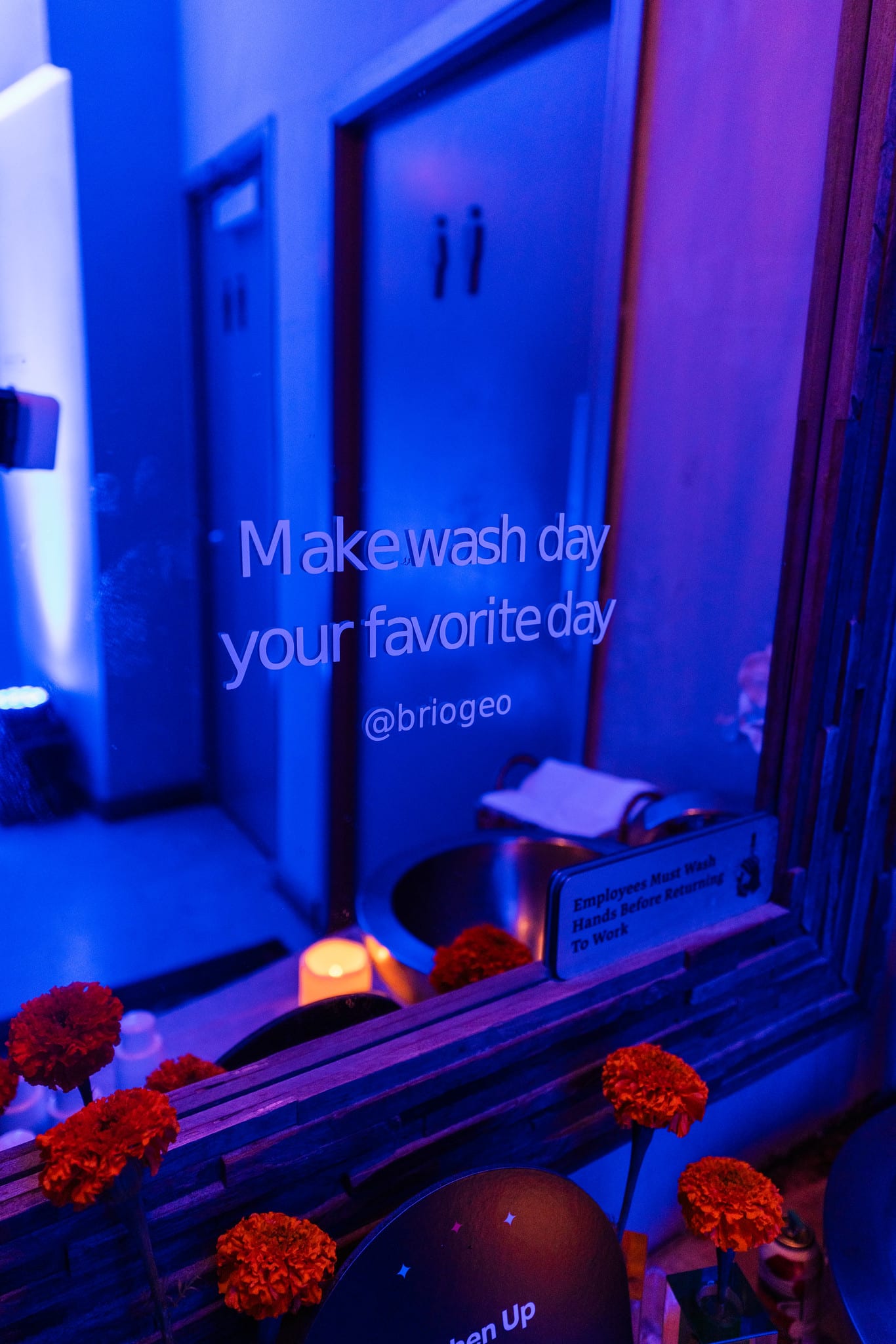 A blue-lit product display reading make wash day your favorite day, from the Briogeo activation at the TikTok and Ulta Beauty #TikTokBeauty dinner on the LouLou rooftop in Santa Monica