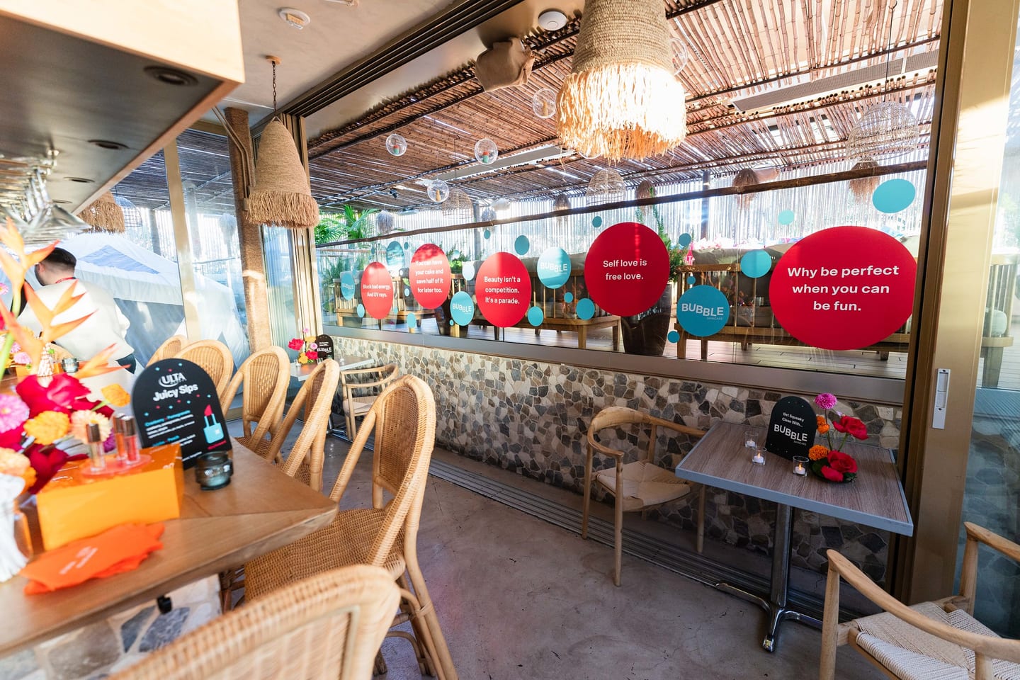 The LouLou rooftop dining room dressed with red and teal Bubble Skincare circle window decals and rattan chairs at the TikTok and Ulta Beauty #TikTokBeauty dinner on the LouLou rooftop in Santa Monica