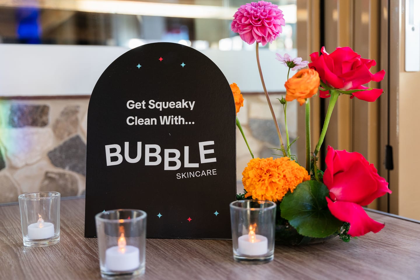 A black table sign reading Get Squeaky Clean With Bubble Skincare, flanked by roses, marigolds and candles at the TikTok and Ulta Beauty #TikTokBeauty dinner on the LouLou rooftop in Santa Monica