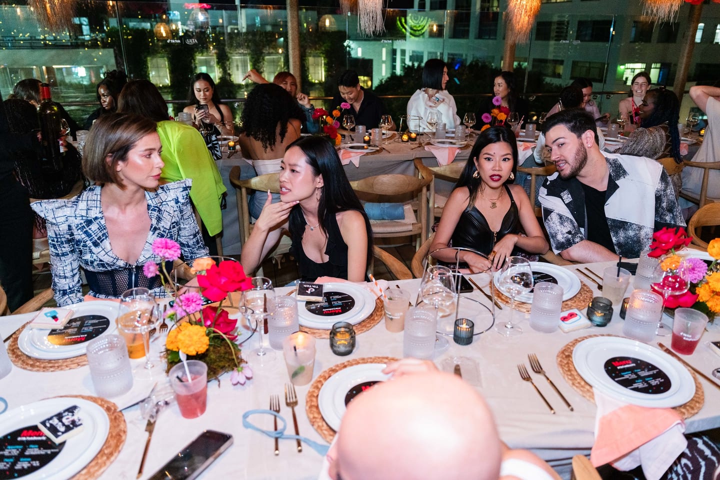 Guests seated along the communal table during dinner under hanging paper flowers at the TikTok and Ulta Beauty #TikTokBeauty dinner on the LouLou rooftop in Santa Monica