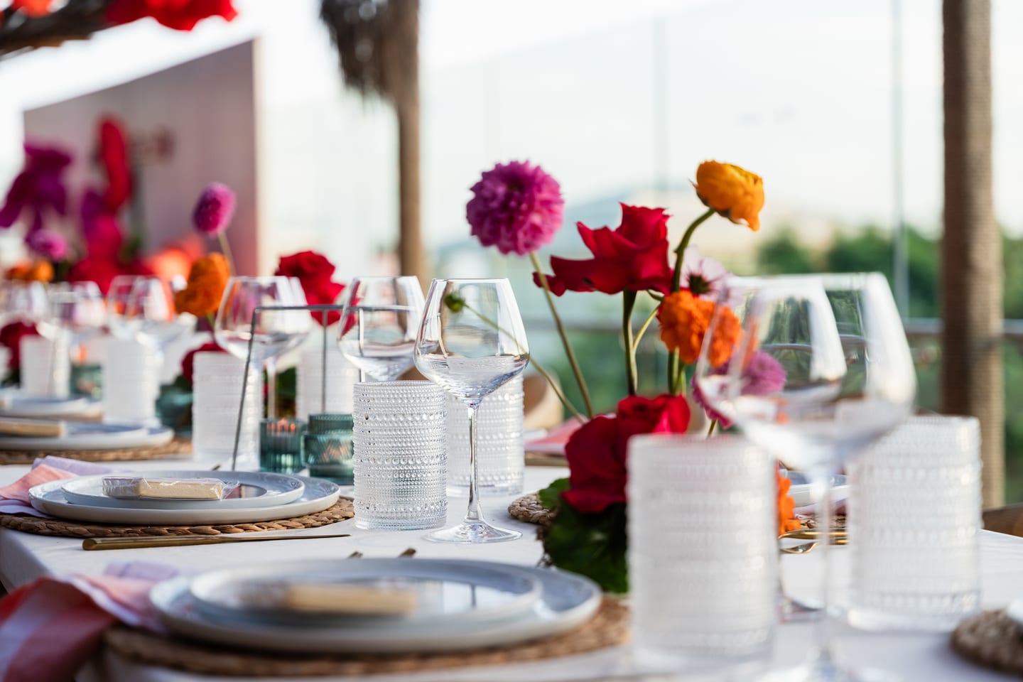 A close view of textured glassware and red and orange ranunculus in bud vases on a set dining table at the TikTok and Ulta Beauty #TikTokBeauty dinner on the LouLou rooftop in Santa Monica