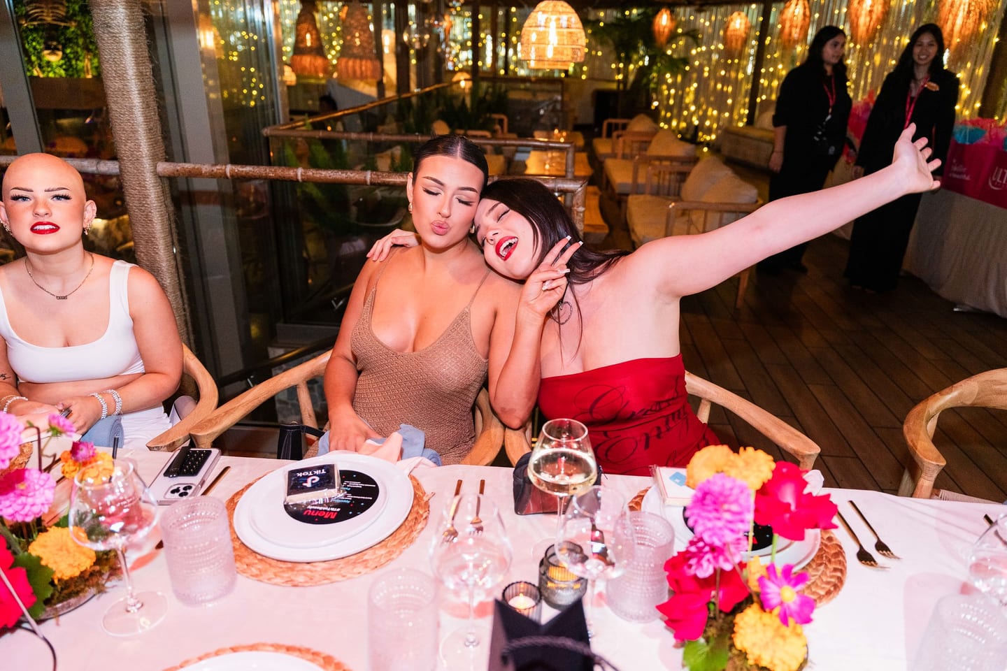 Three guests being playful at the dinner table, one with an arm outstretched at the TikTok and Ulta Beauty #TikTokBeauty dinner on the LouLou rooftop in Santa Monica