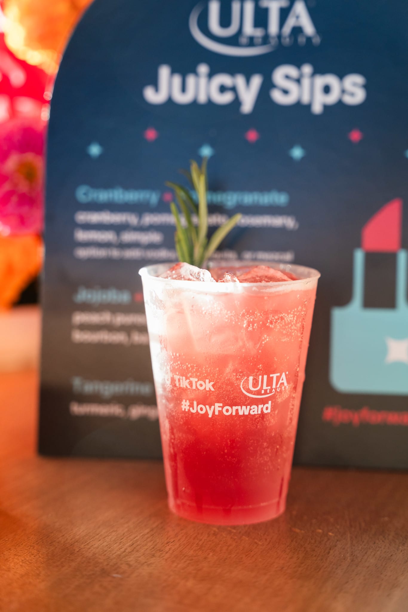A red cranberry and pomegranate cocktail garnished with rosemary in front of an Ulta Beauty Juicy Sips menu card at the TikTok and Ulta Beauty #TikTokBeauty dinner on the LouLou rooftop in Santa Monica