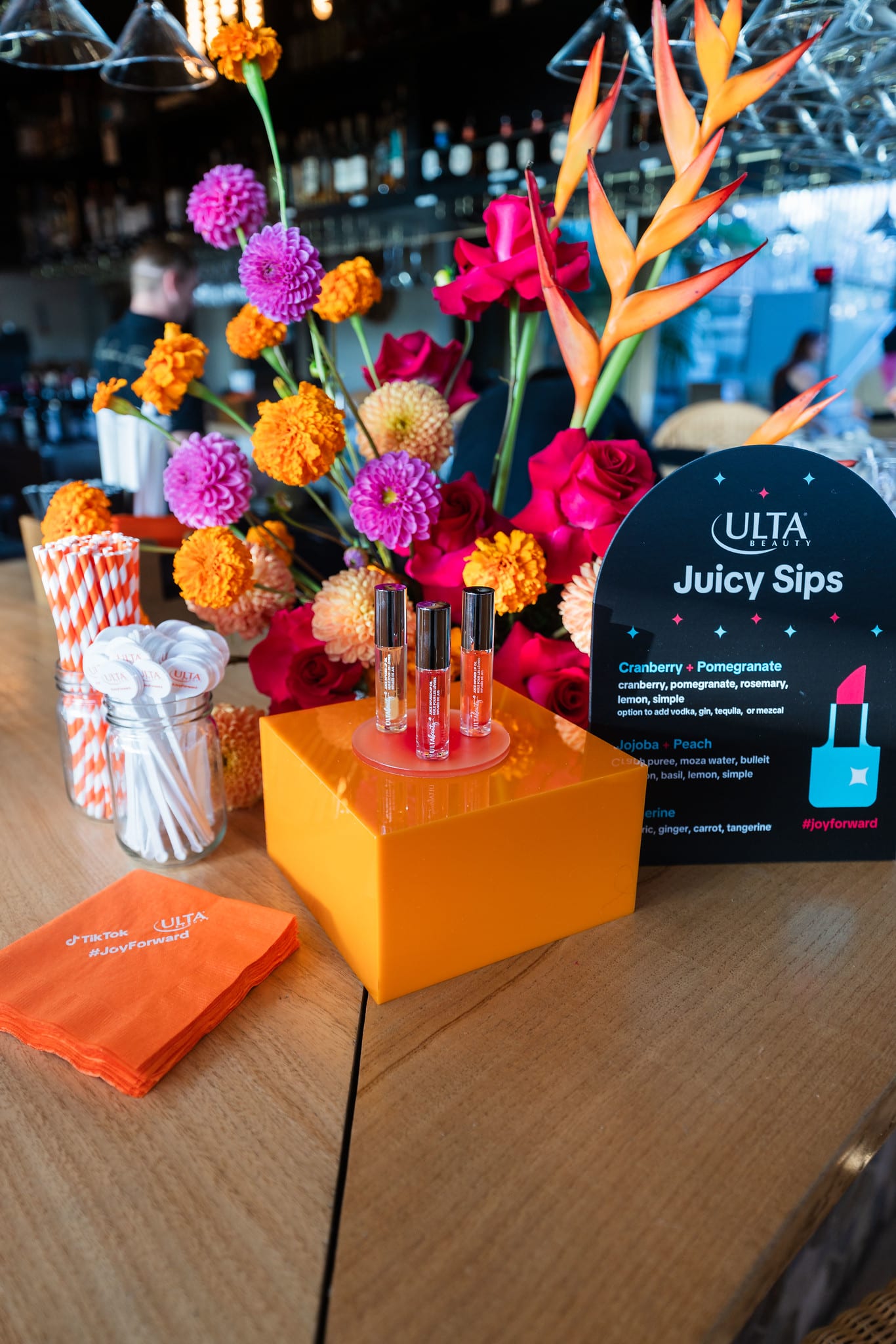 An orange pedestal styled with bright florals and an Ulta Beauty Juicy Sips menu card at the TikTok and Ulta Beauty #TikTokBeauty dinner on the LouLou rooftop in Santa Monica