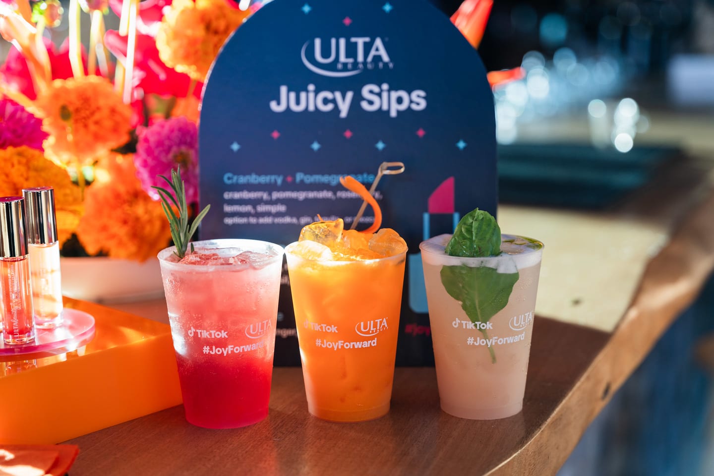 Three branded cocktails in clear cups in front of an Ulta Beauty Juicy Sips menu card at the TikTok and Ulta Beauty #TikTokBeauty dinner on the LouLou rooftop in Santa Monica