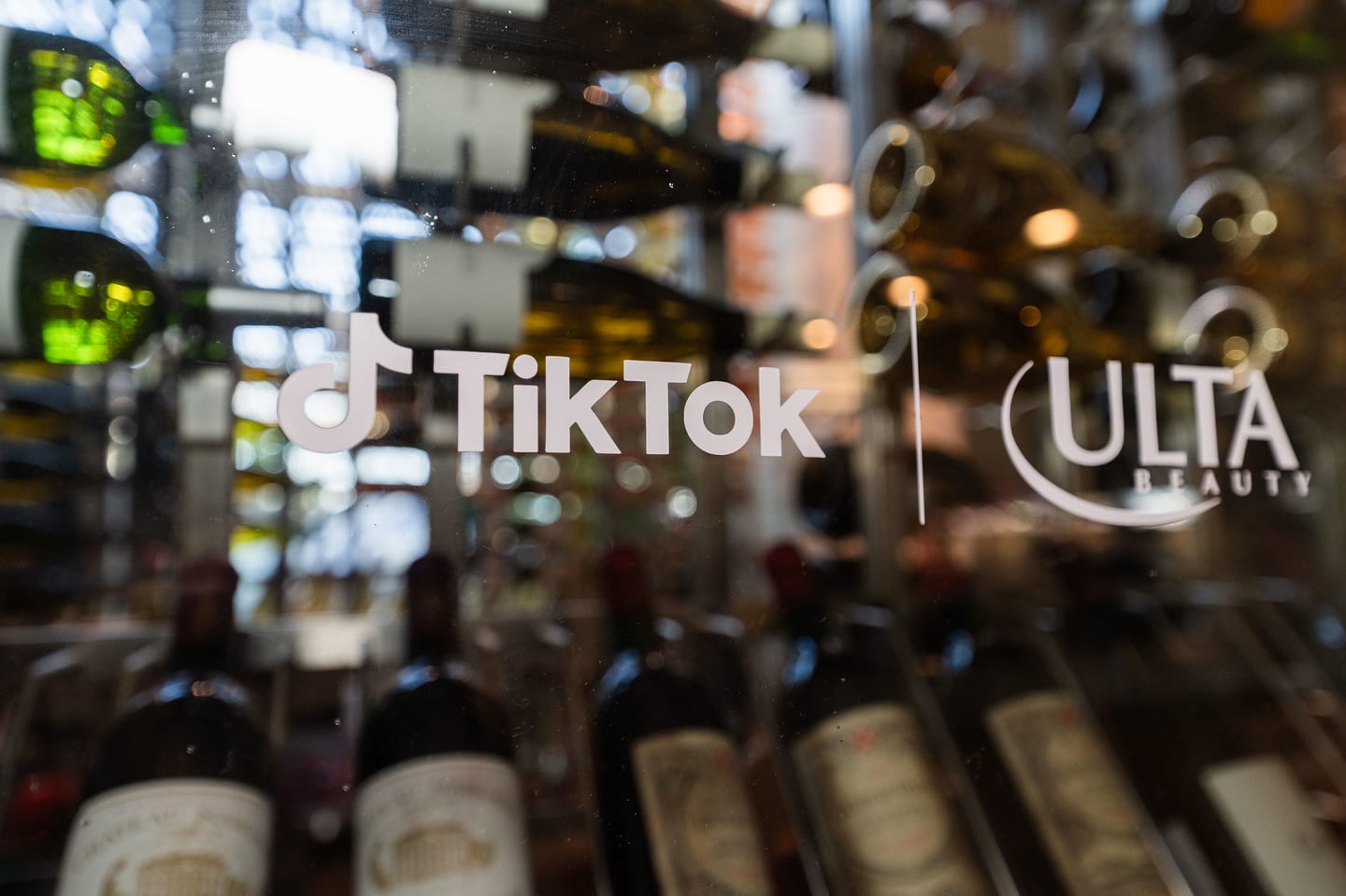 A backlit TikTok and Ulta Beauty logo lockup seen through hanging bar glassware at the TikTok and Ulta Beauty #TikTokBeauty dinner on the LouLou rooftop in Santa Monica