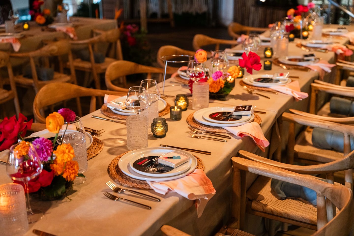 A long communal table set with woven chargers, gold flatware and low floral arrangements, seen down its length at the TikTok and Ulta Beauty #TikTokBeauty dinner on the LouLou rooftop in Santa Monica