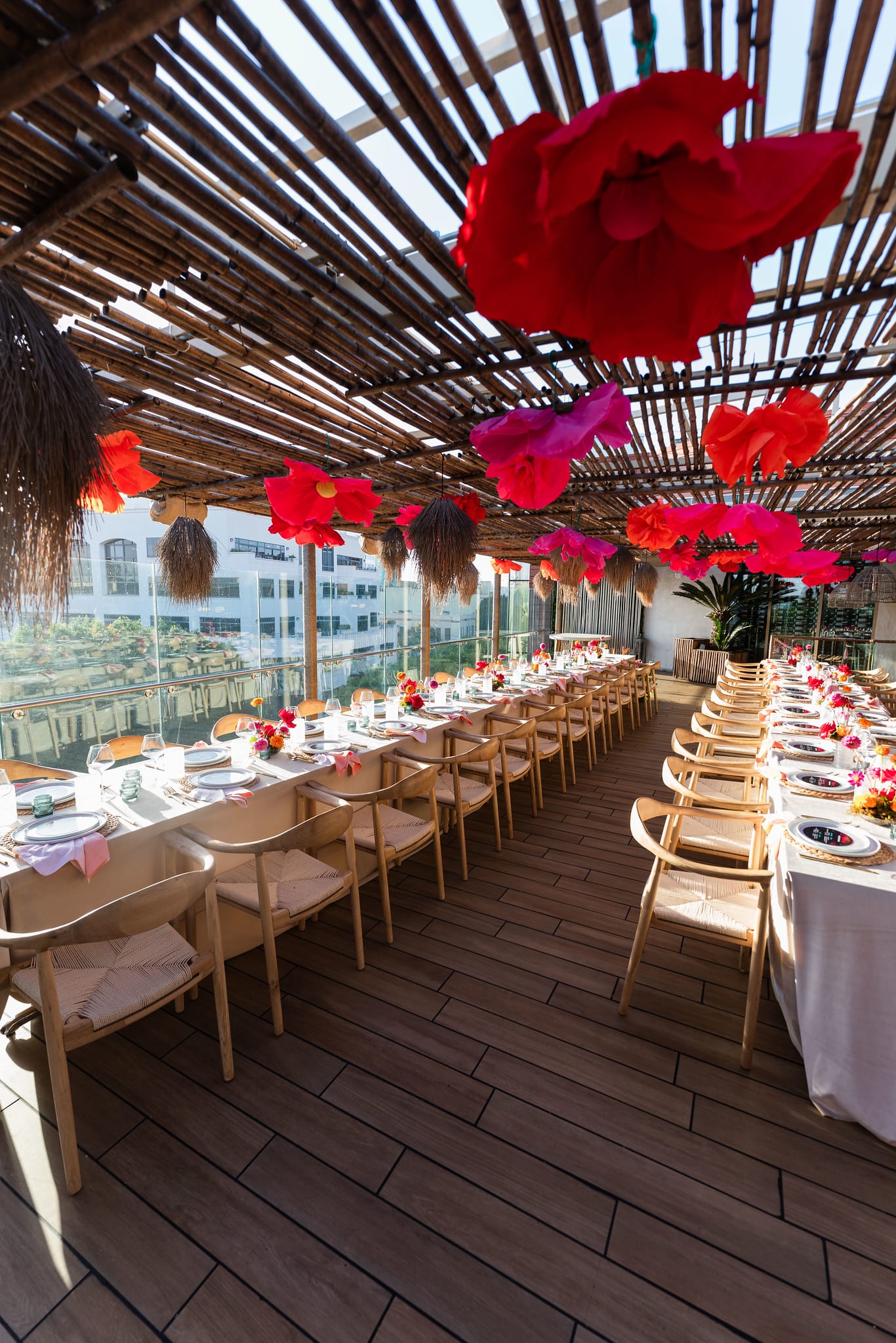Oversized red and pink paper flowers suspended from the slatted rooftop ceiling above a set dining table at the TikTok and Ulta Beauty #TikTokBeauty dinner on the LouLou rooftop in Santa Monica