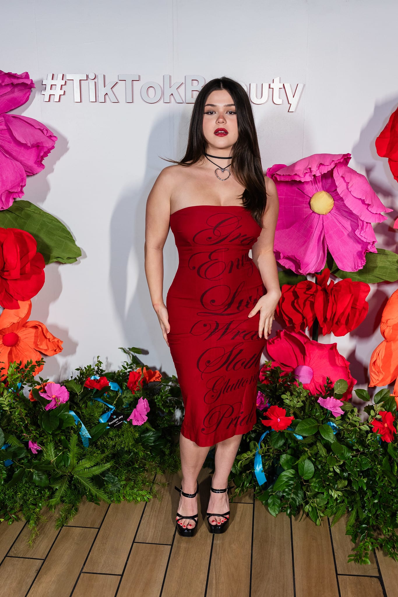 A guest in a red dress posing at the oversized floral #TikTokBeauty backdrop at the TikTok and Ulta Beauty #TikTokBeauty dinner on the LouLou rooftop in Santa Monica