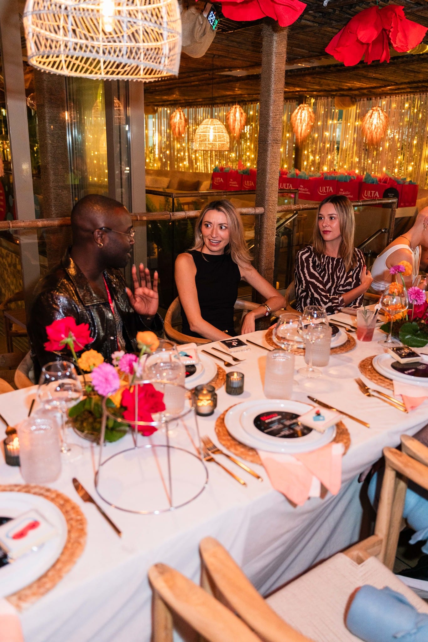 Guests seated around the rooftop table under hanging lanterns during dinner at the TikTok and Ulta Beauty #TikTokBeauty dinner on the LouLou rooftop in Santa Monica