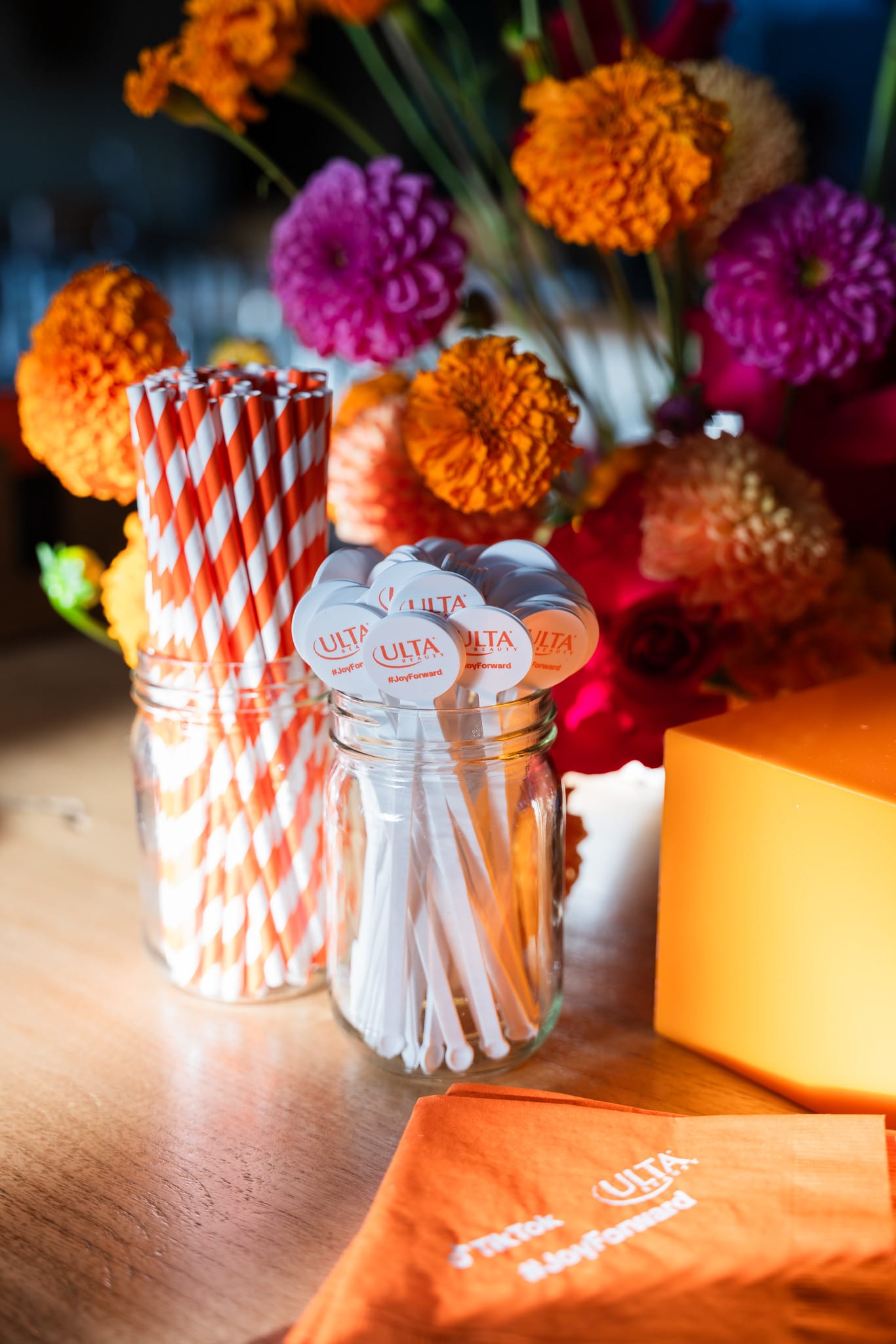 Striped paper straws in a cup beside orange marigolds and dahlias on a branded surface at the TikTok and Ulta Beauty #TikTokBeauty dinner on the LouLou rooftop in Santa Monica