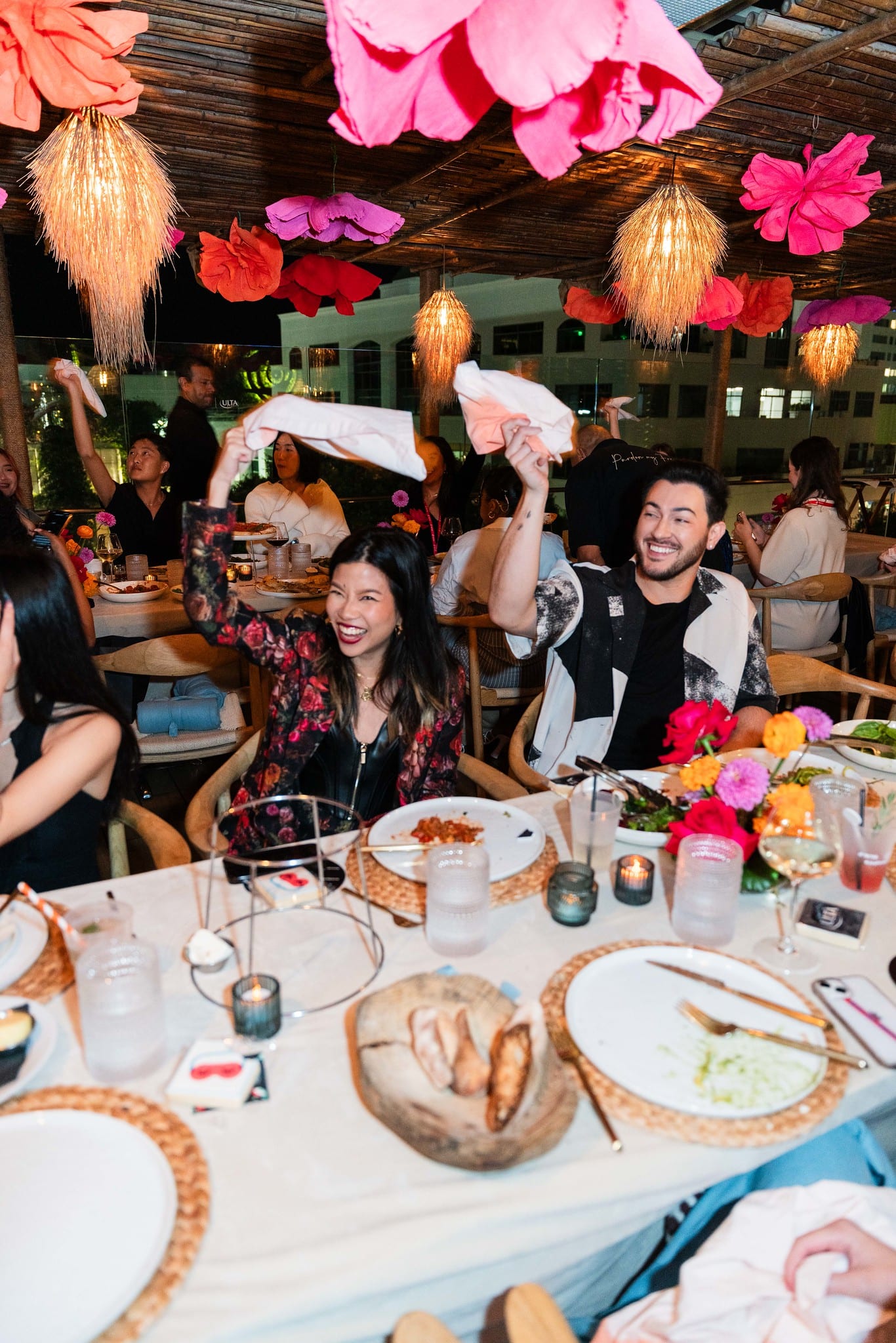 Guests seated at dinner beneath oversized hanging paper flowers at the TikTok and Ulta Beauty #TikTokBeauty dinner on the LouLou rooftop in Santa Monica