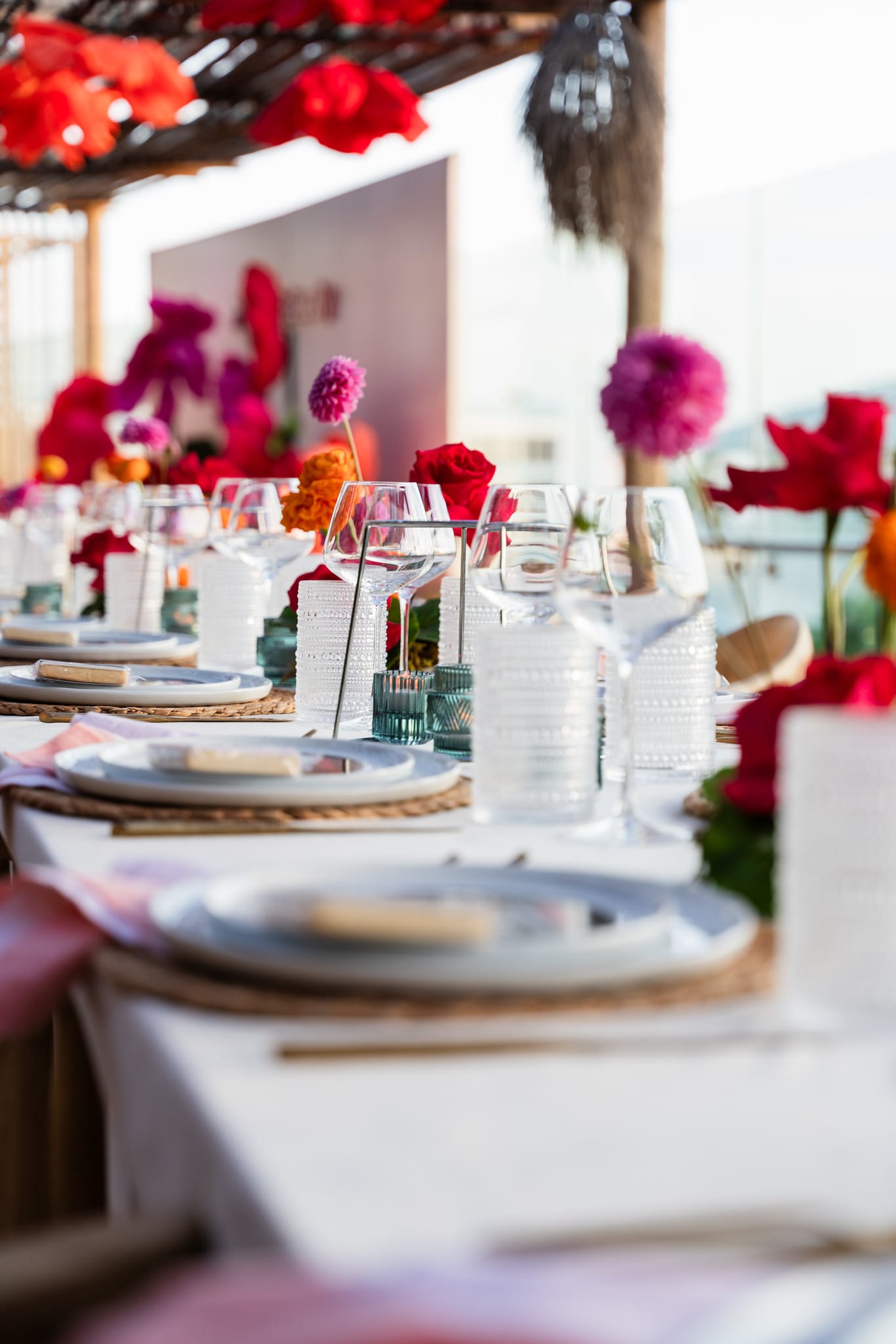 A detail of white plates, gold flatware and bright pink and red paper flowers on a set dining table at the TikTok and Ulta Beauty #TikTokBeauty dinner on the LouLou rooftop in Santa Monica