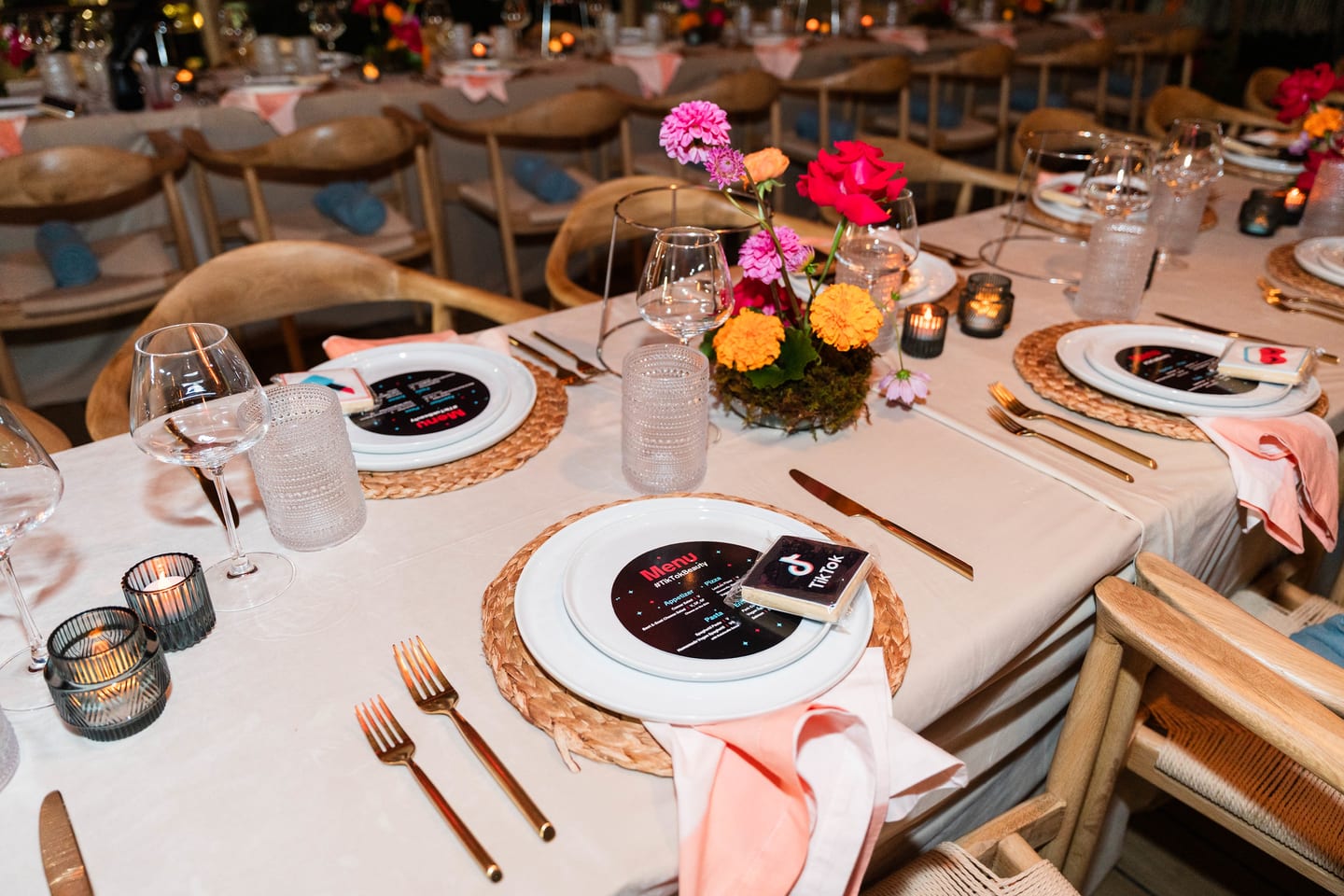 A set table with pink linen napkins, gold flatware, candles and orange and red floral arrangements at the TikTok and Ulta Beauty #TikTokBeauty dinner on the LouLou rooftop in Santa Monica