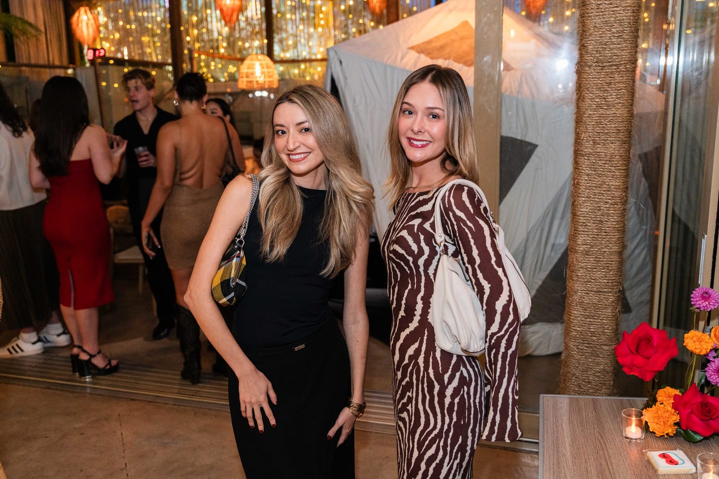 Two guests posing together with the party going on behind them at the TikTok and Ulta Beauty #TikTokBeauty dinner on the LouLou rooftop in Santa Monica