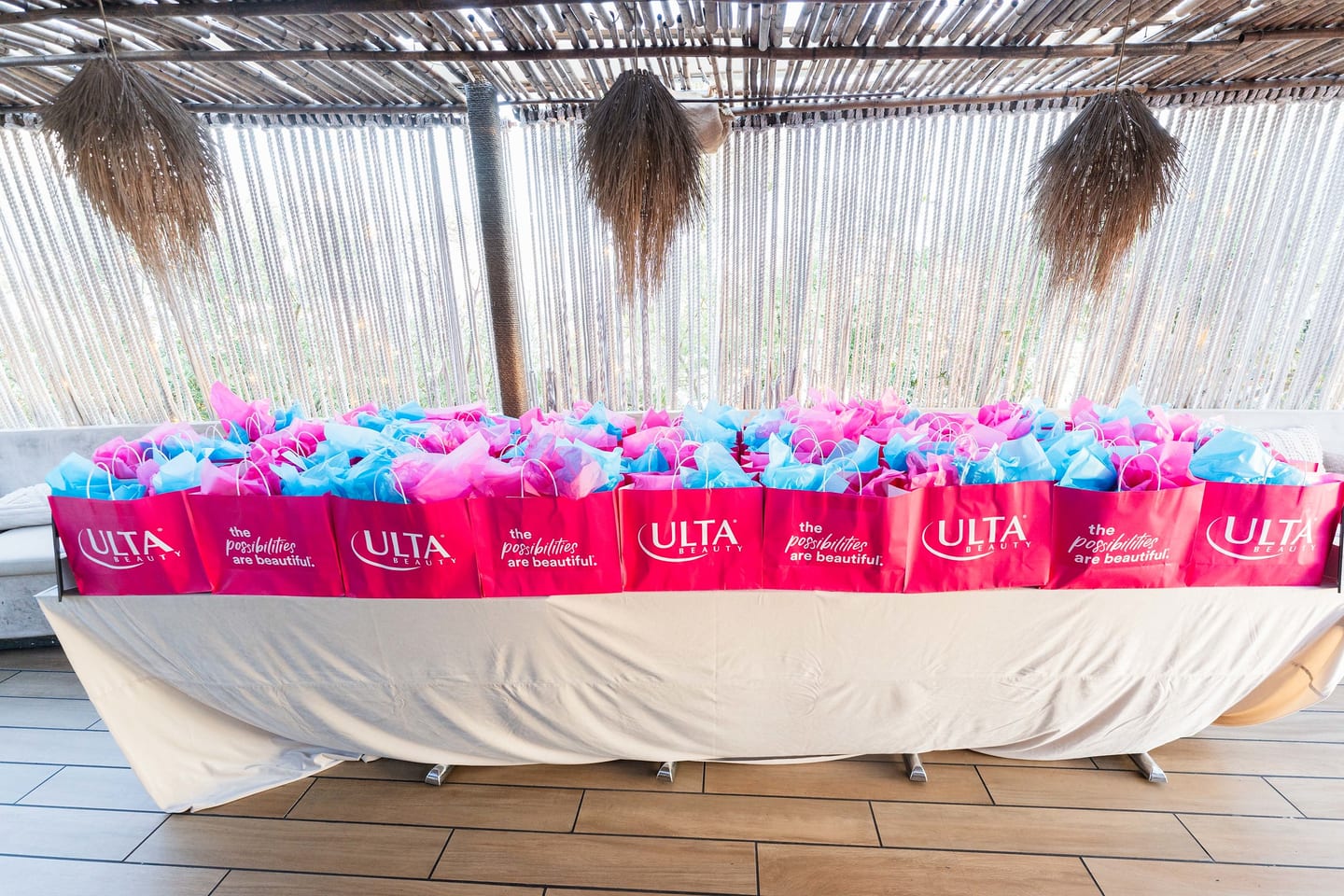 A long table lined with pink Ulta Beauty gift bags stuffed with blue tissue at the TikTok and Ulta Beauty #TikTokBeauty dinner on the LouLou rooftop in Santa Monica