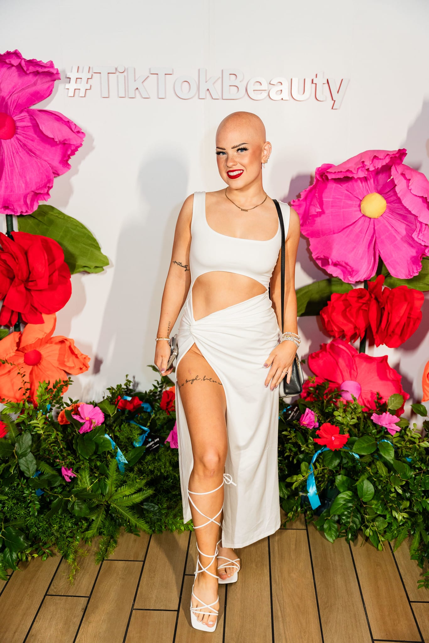 A guest in a white outfit posing at the oversized floral #TikTokBeauty backdrop at the TikTok and Ulta Beauty #TikTokBeauty dinner on the LouLou rooftop in Santa Monica