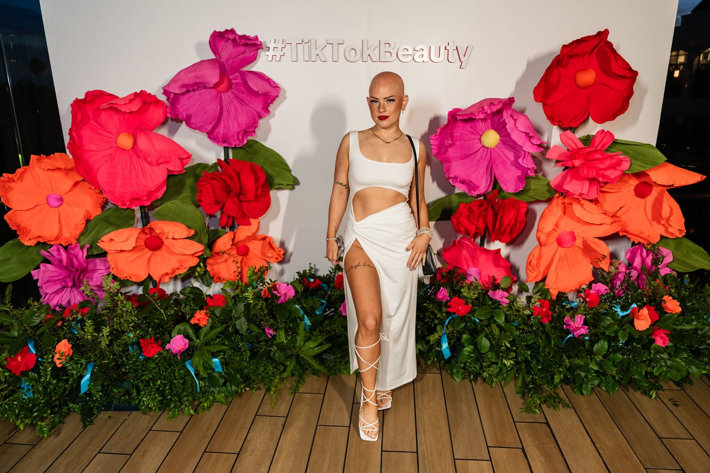 A full-length frame of a guest in a white look walking the floral #TikTokBeauty step-and-repeat at the TikTok and Ulta Beauty #TikTokBeauty dinner on the LouLou rooftop in Santa Monica