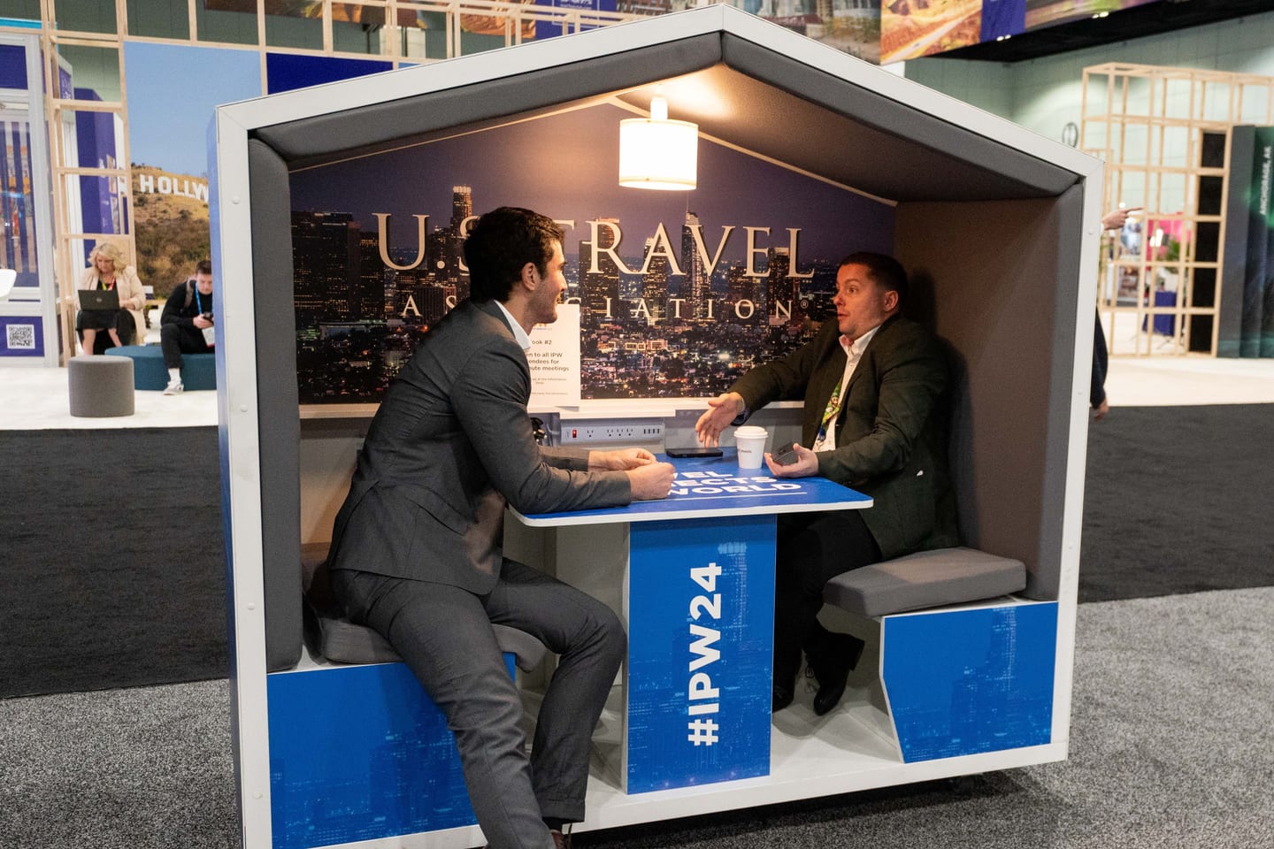 Two attendees meeting inside a U.S. Travel branded meeting pod on the IPW trade show floor